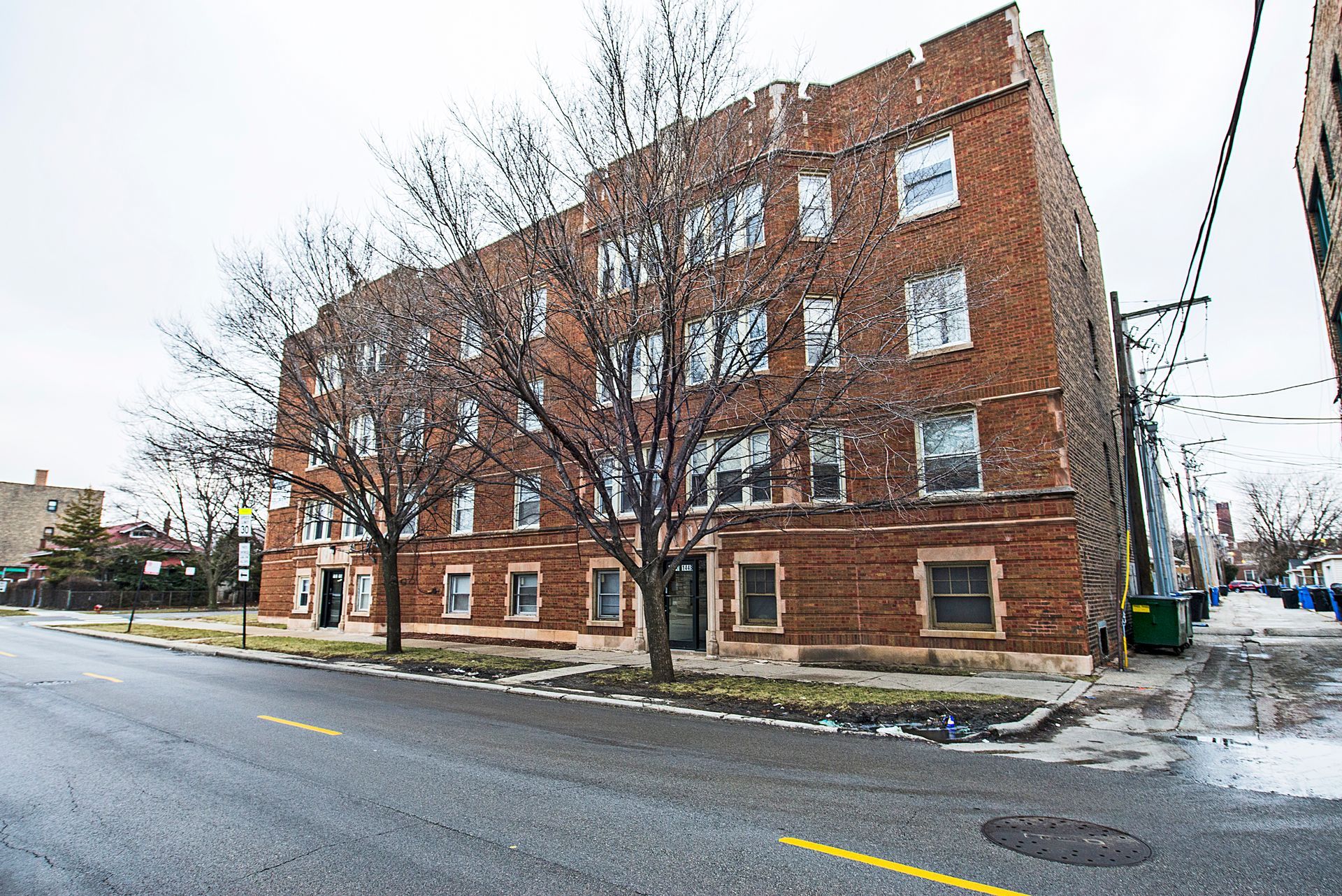 Brick apartment building on a street, bare trees, overcast sky.