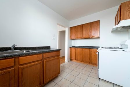 Kitchen with wood cabinets, dark countertops, white appliances, and tiled floor.