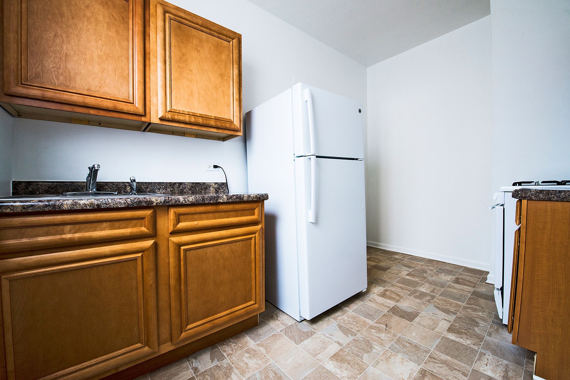 Kitchen with brown cabinets, white refrigerator, and patterned floor.
