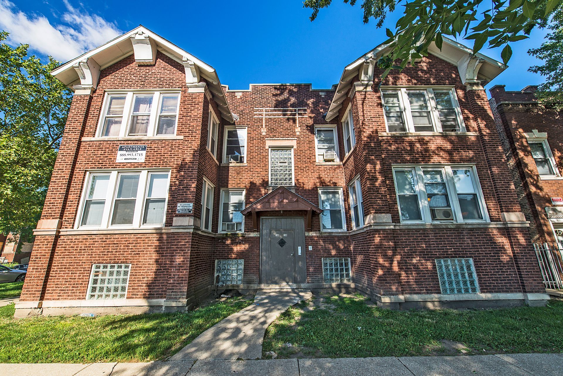Brick two-story apartment building with several windows, a small front yard, and a clear blue sky.