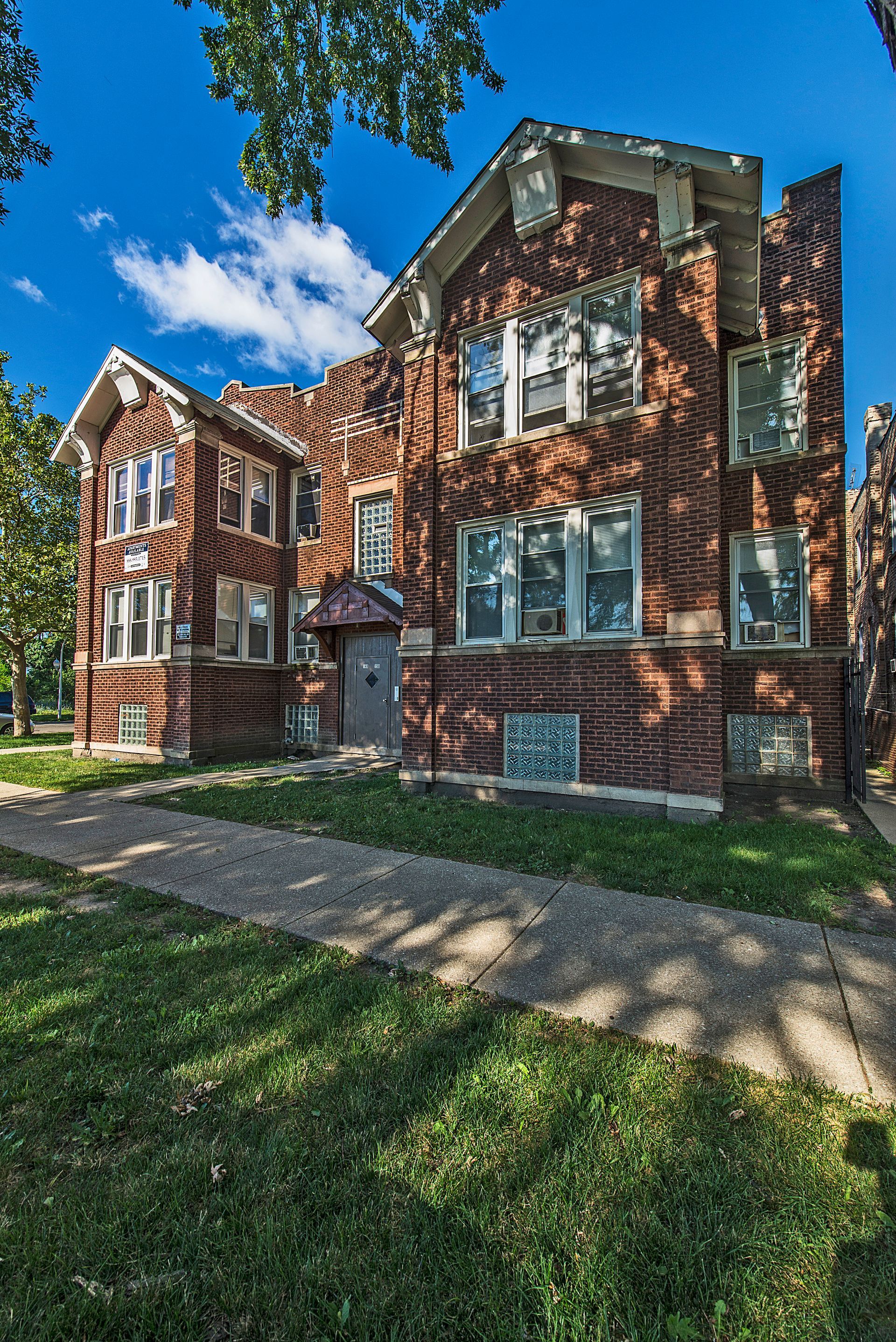 Brick multi-family building with multiple windows, blue sky background.
