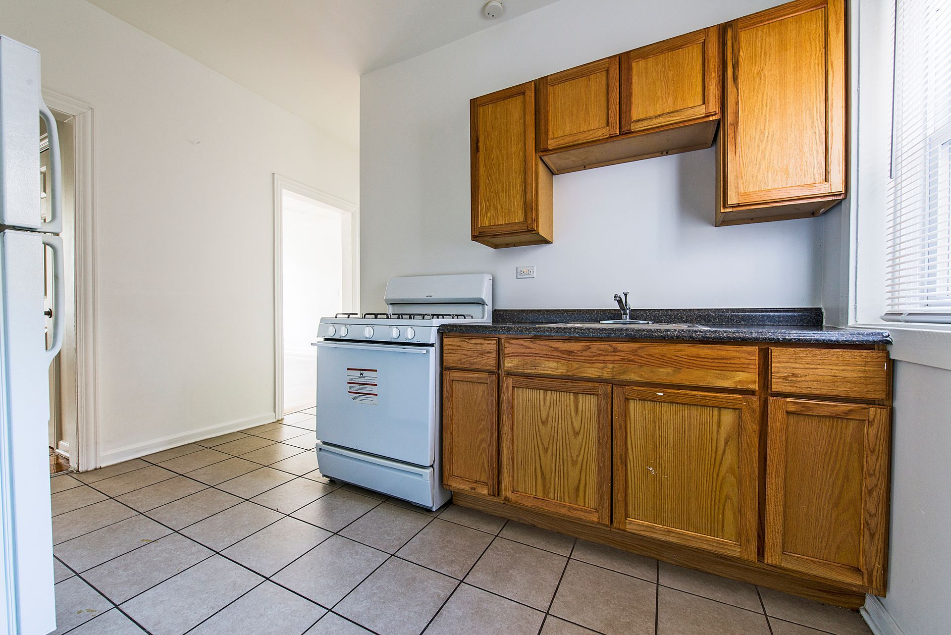 Kitchen with wooden cabinets, stove, sink, and tiled floor.