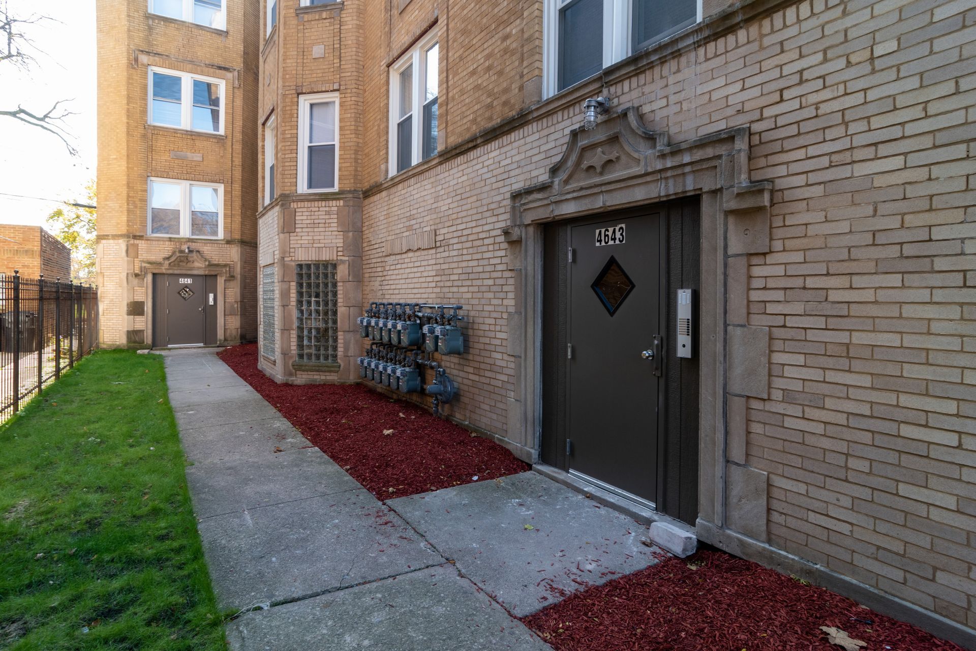 Exterior of brick apartment building with entryway and red mulch border.