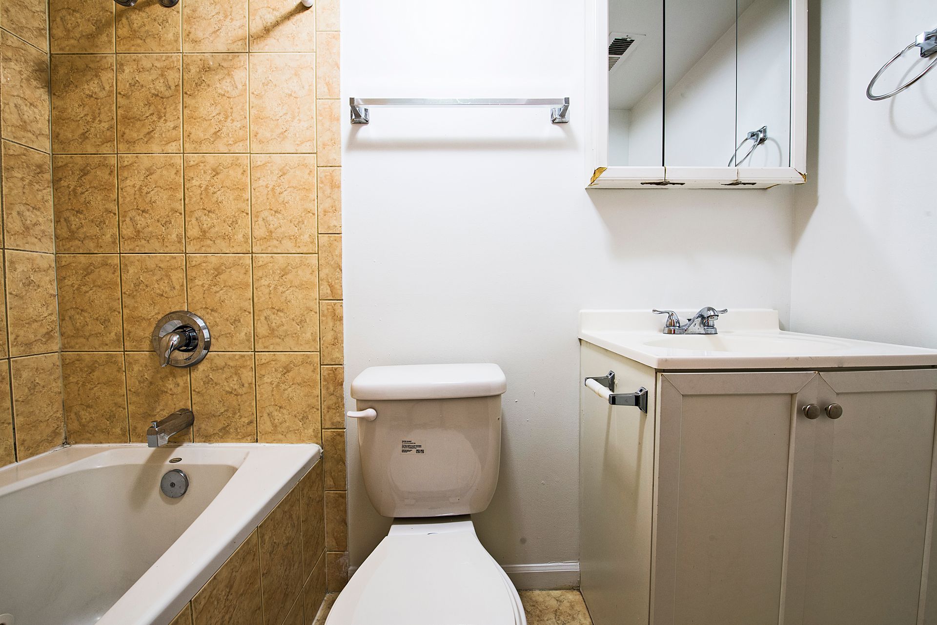 Bathroom with a toilet, tub, vanity, and beige tile. White walls and a medicine cabinet are present.