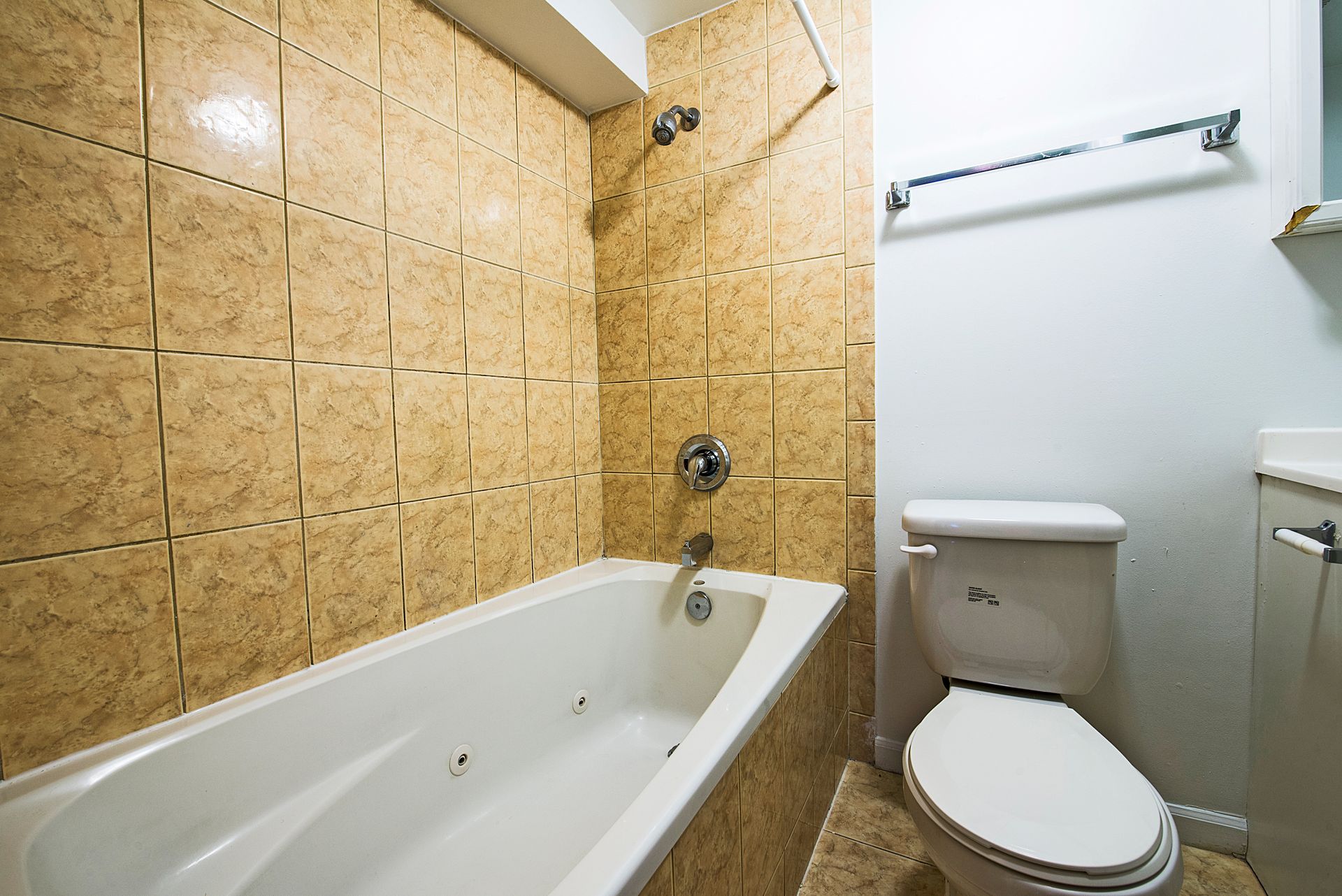 Bathroom with a white bathtub, toilet, and beige tile shower walls.