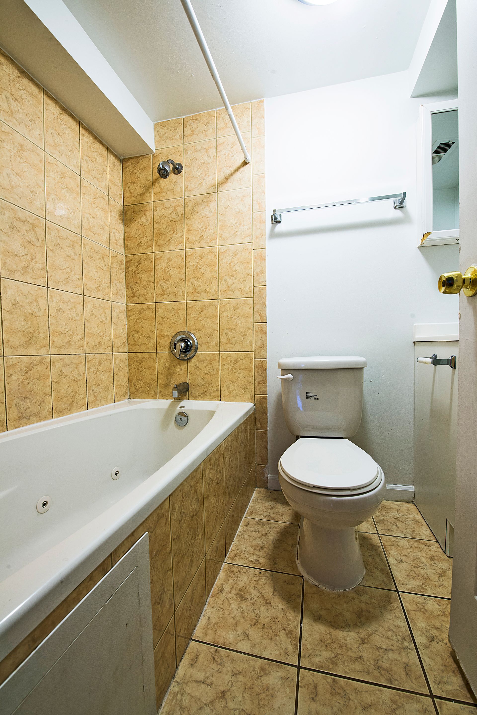 Bathroom with a bathtub, toilet, and tan tile walls and floor.