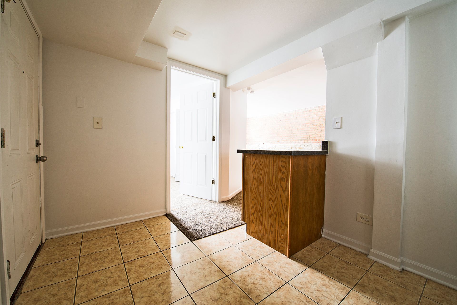 Interior with a tile floor, white walls, open door, and a wood cabinet.
