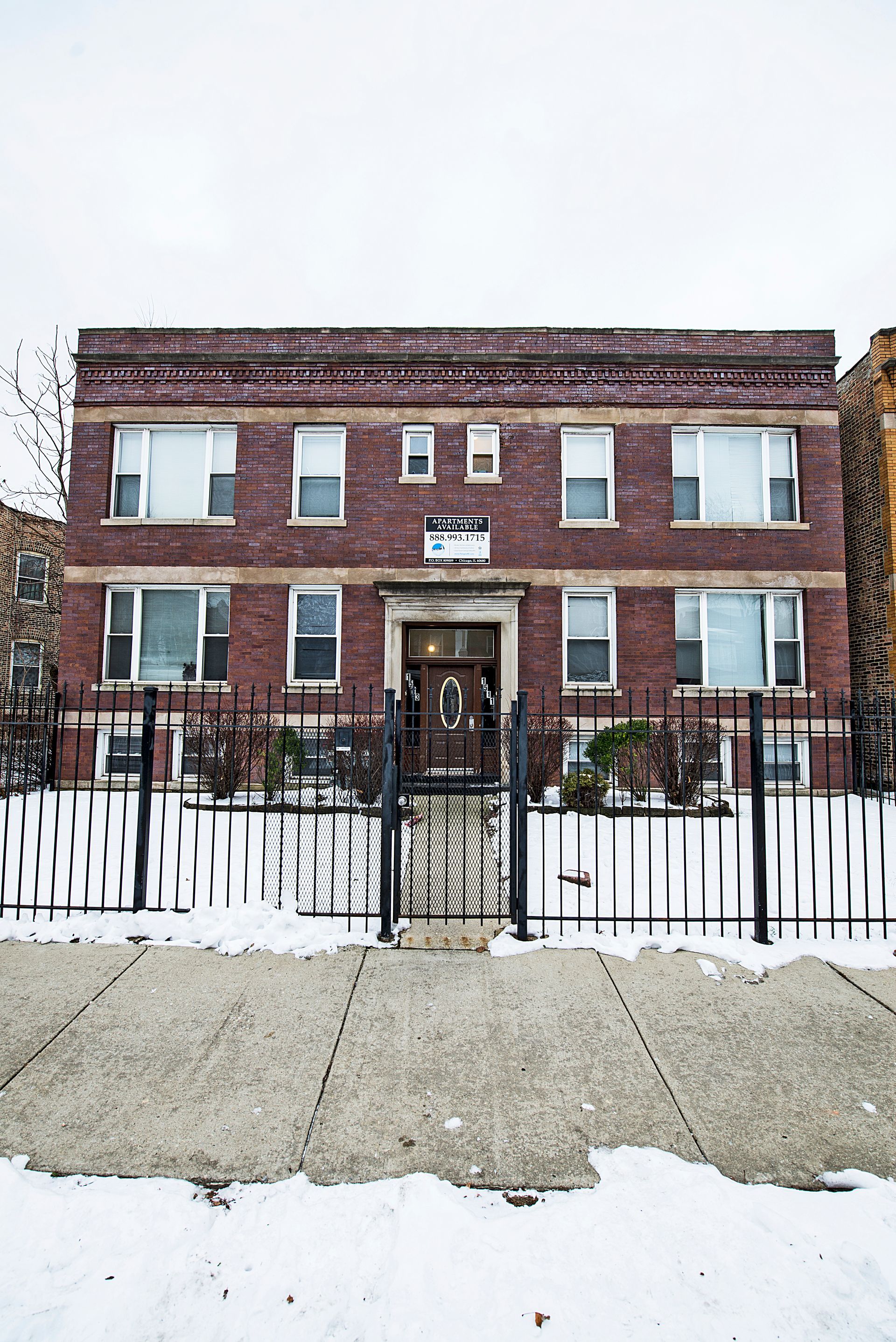 Red brick apartment building with white picket fence and snow-covered ground.