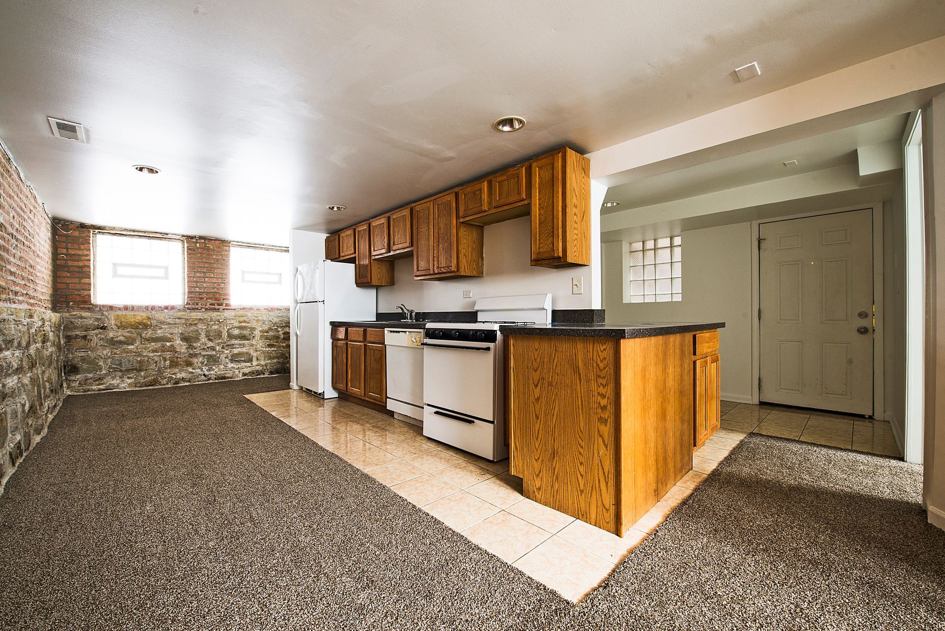 Kitchen with cabinets, white appliances, and a stone wall. Brown cabinets, speckled floor.