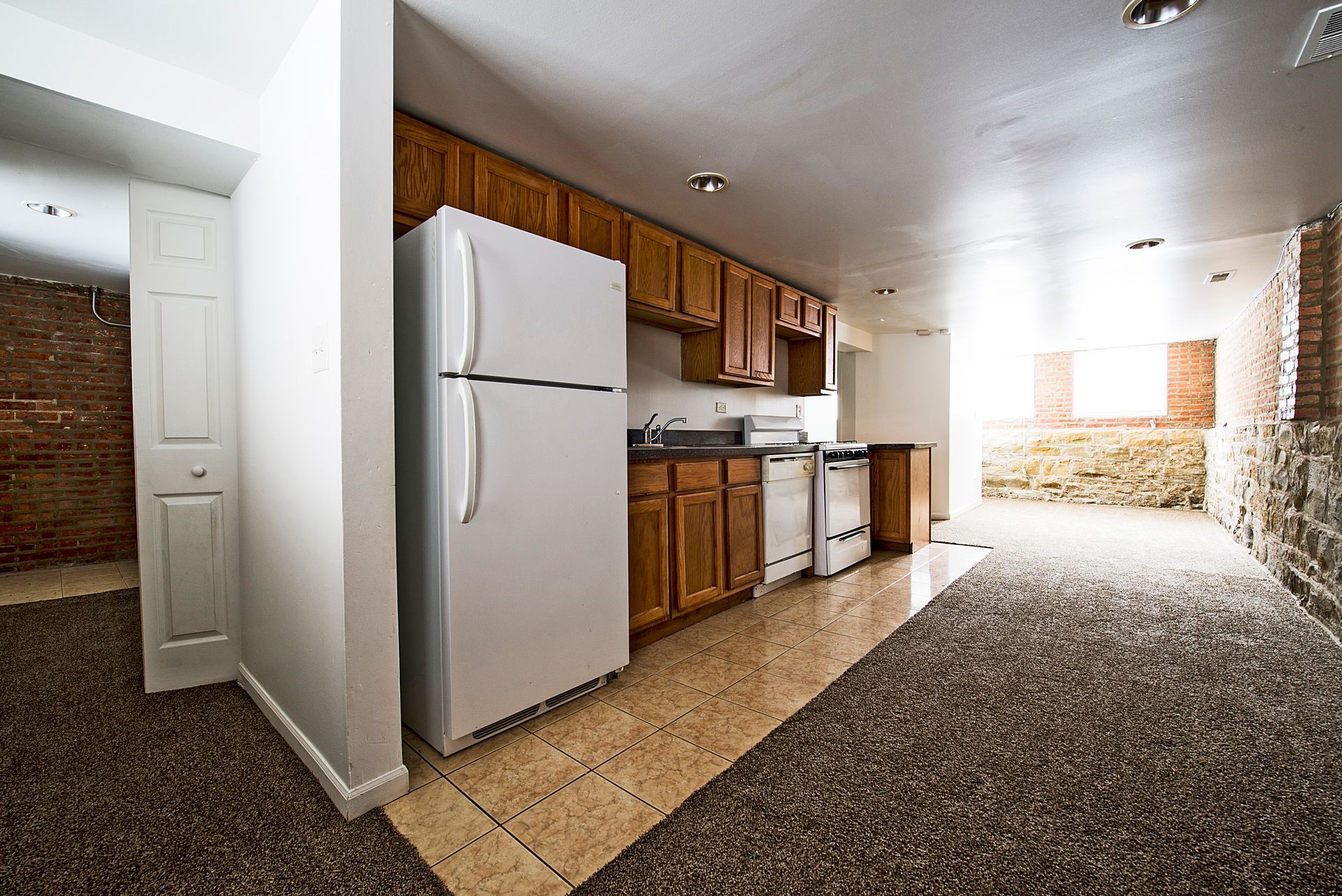 Kitchen with white refrigerator, brown cabinets, and brick and stone walls.