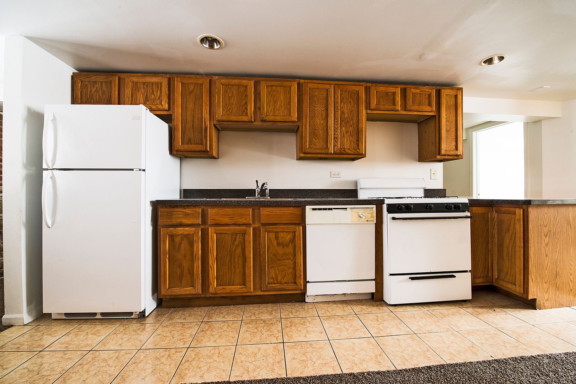 Kitchen with brown cabinets, white appliances, and tiled floor.