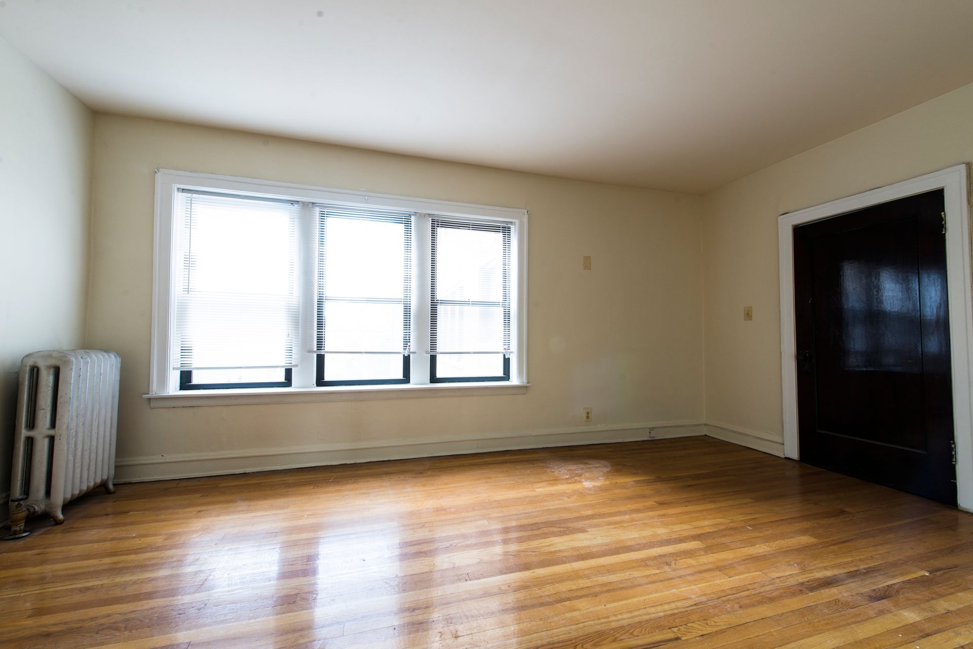 Empty room with wood floor, window with blinds, and a radiator.