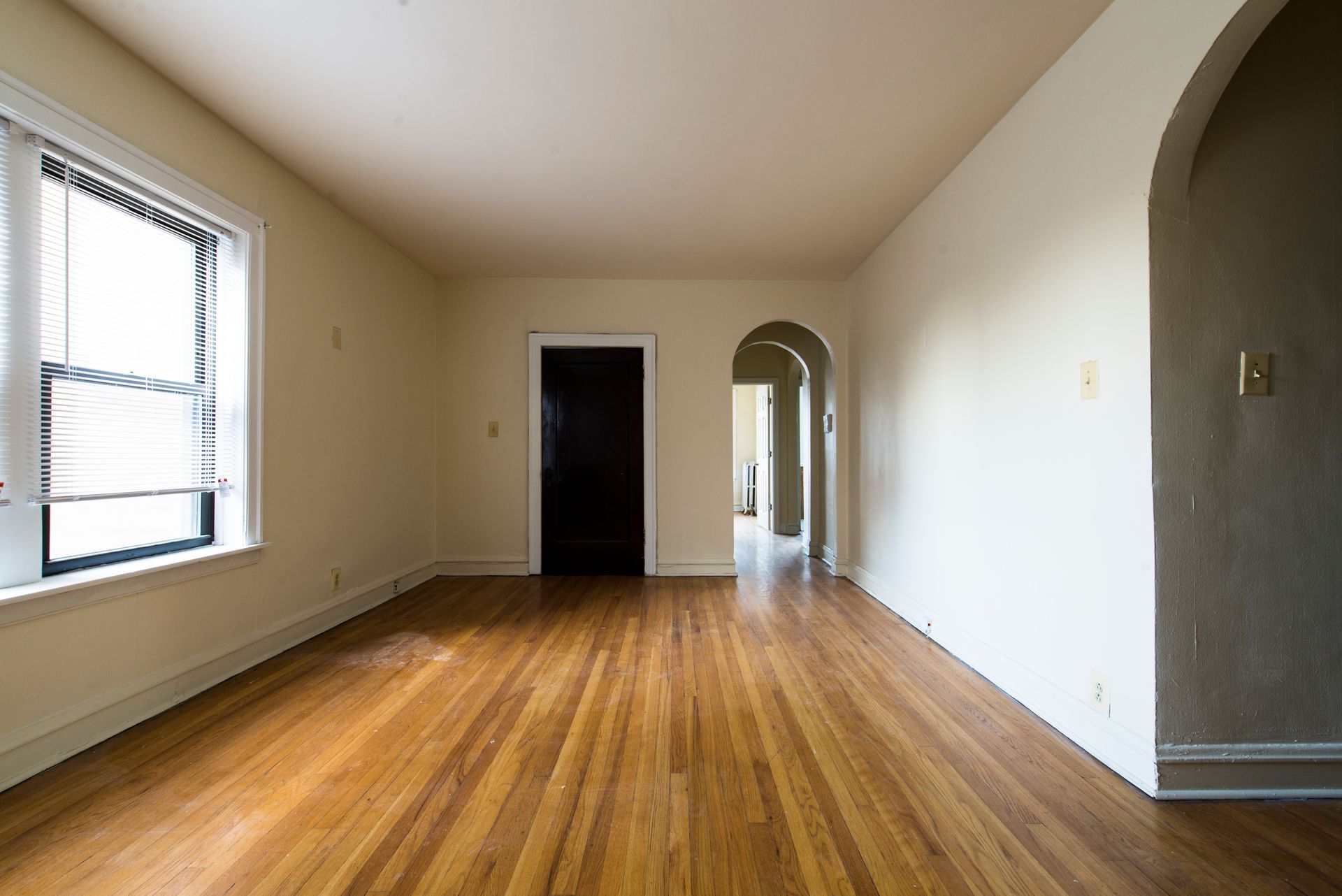 Empty room with hardwood floors, a window, and arched doorways.