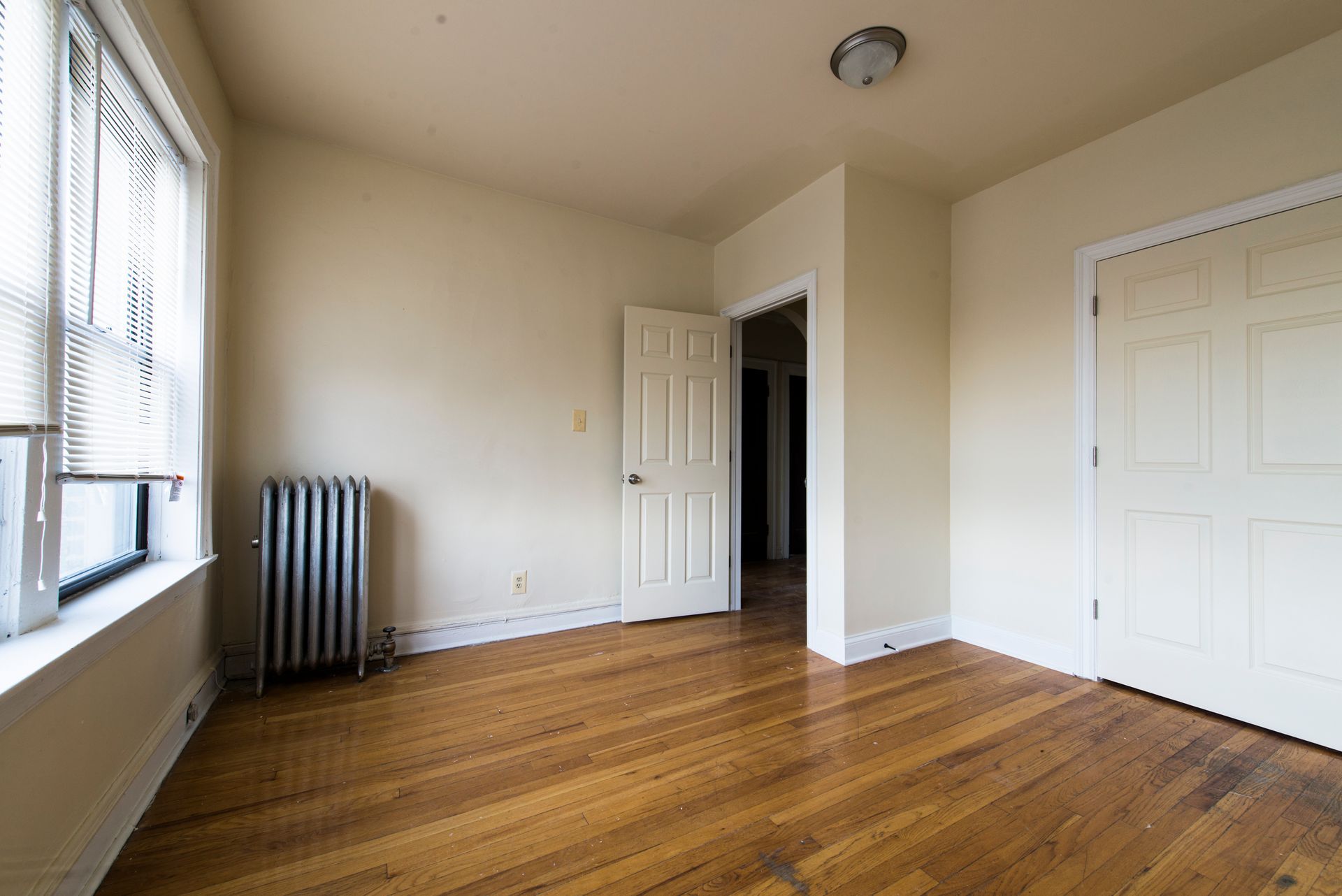 Empty room with hardwood floors, a radiator, window, open doorway, and closet.