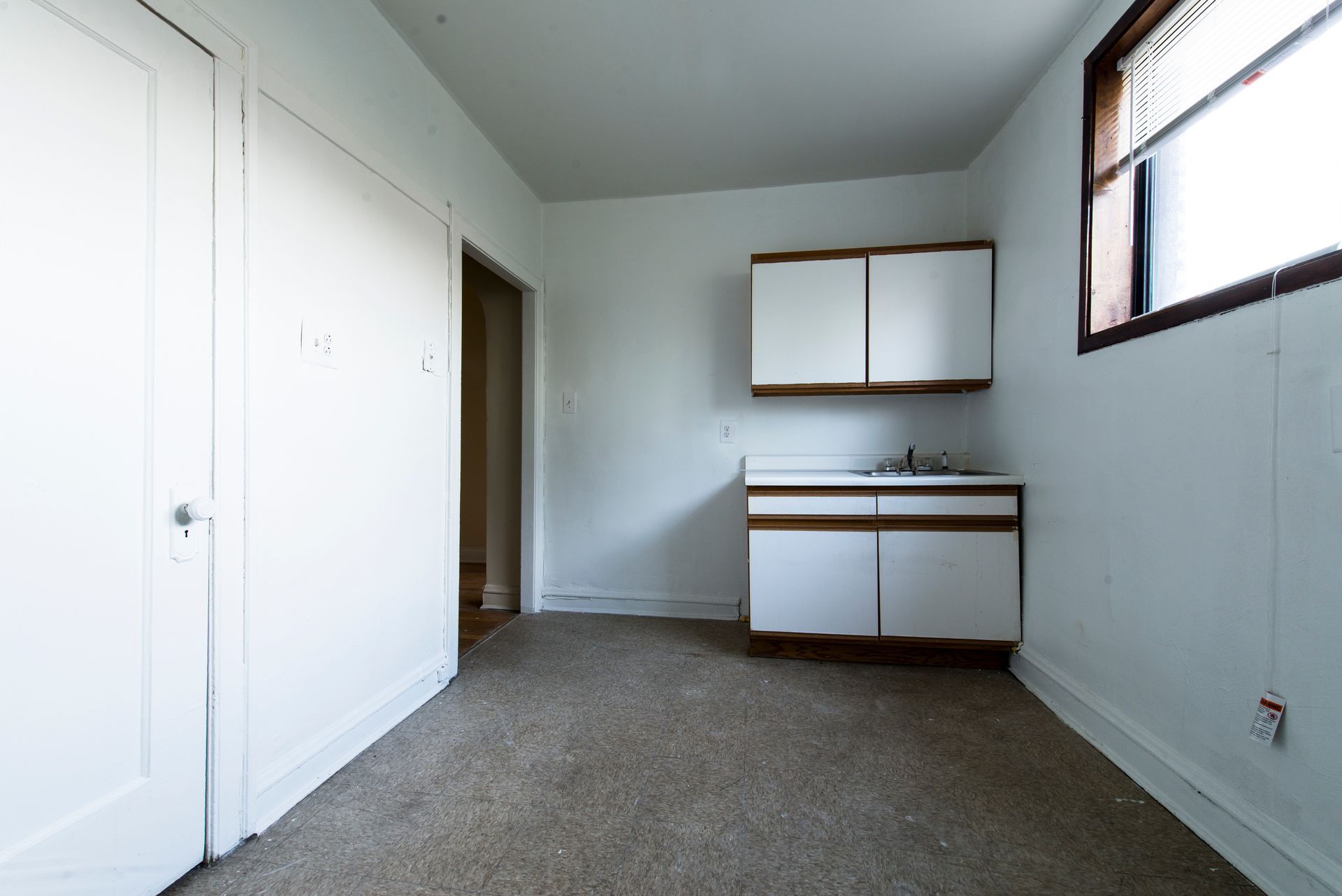 Empty white room with cabinets, sink, and window.