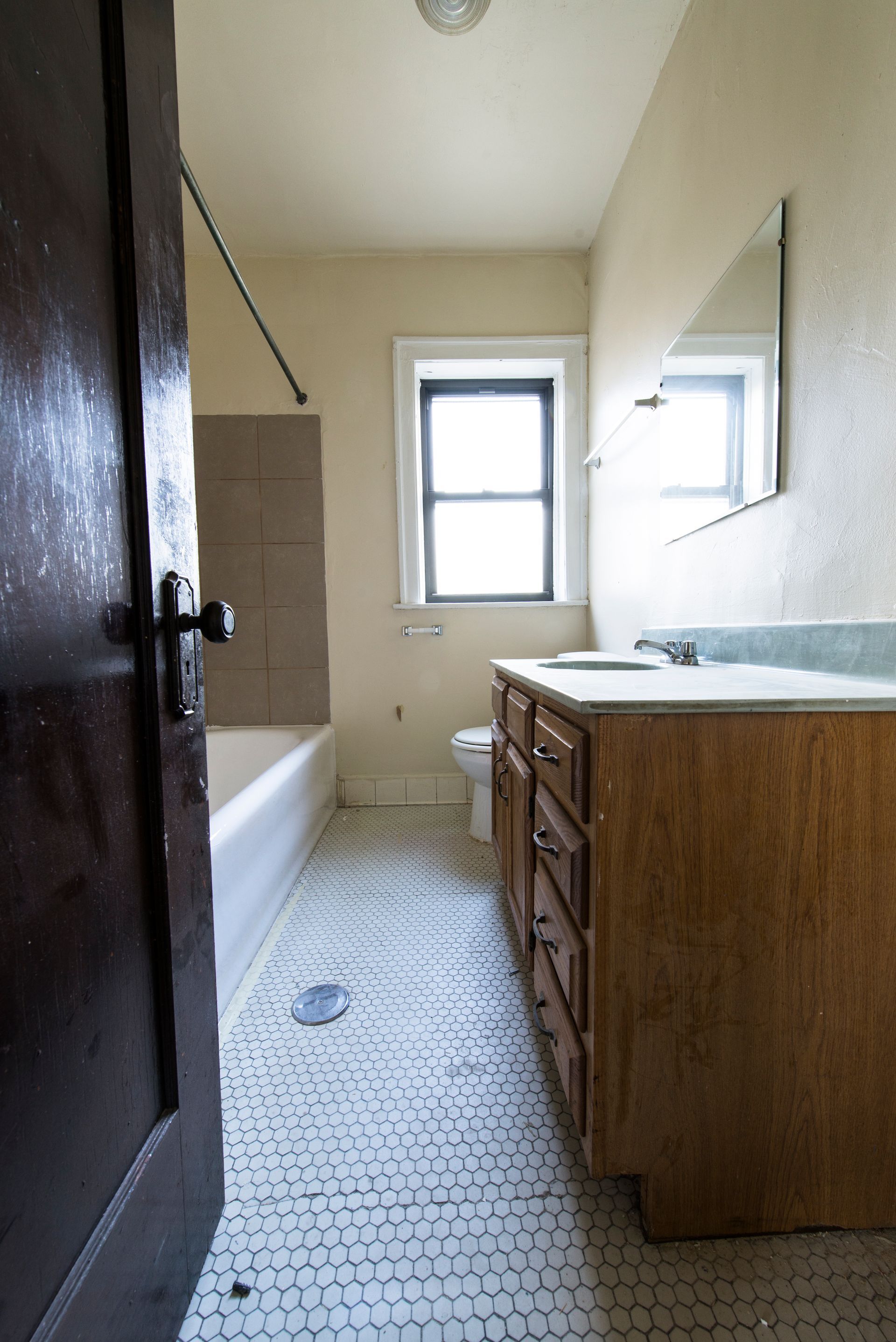 Bathroom with vanity, toilet, and bathtub. Beige walls, wood cabinets, and hexagon tile floor.