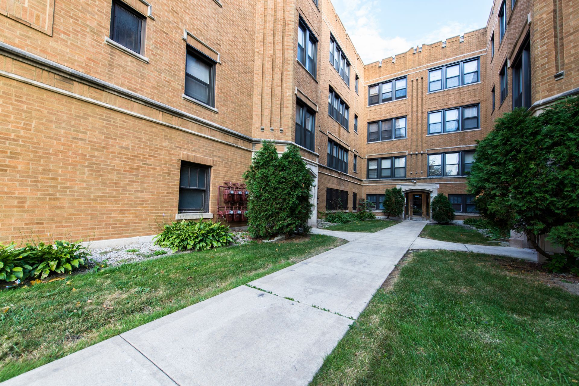 Courtyard of a brick apartment building with a concrete walkway and green landscaping.