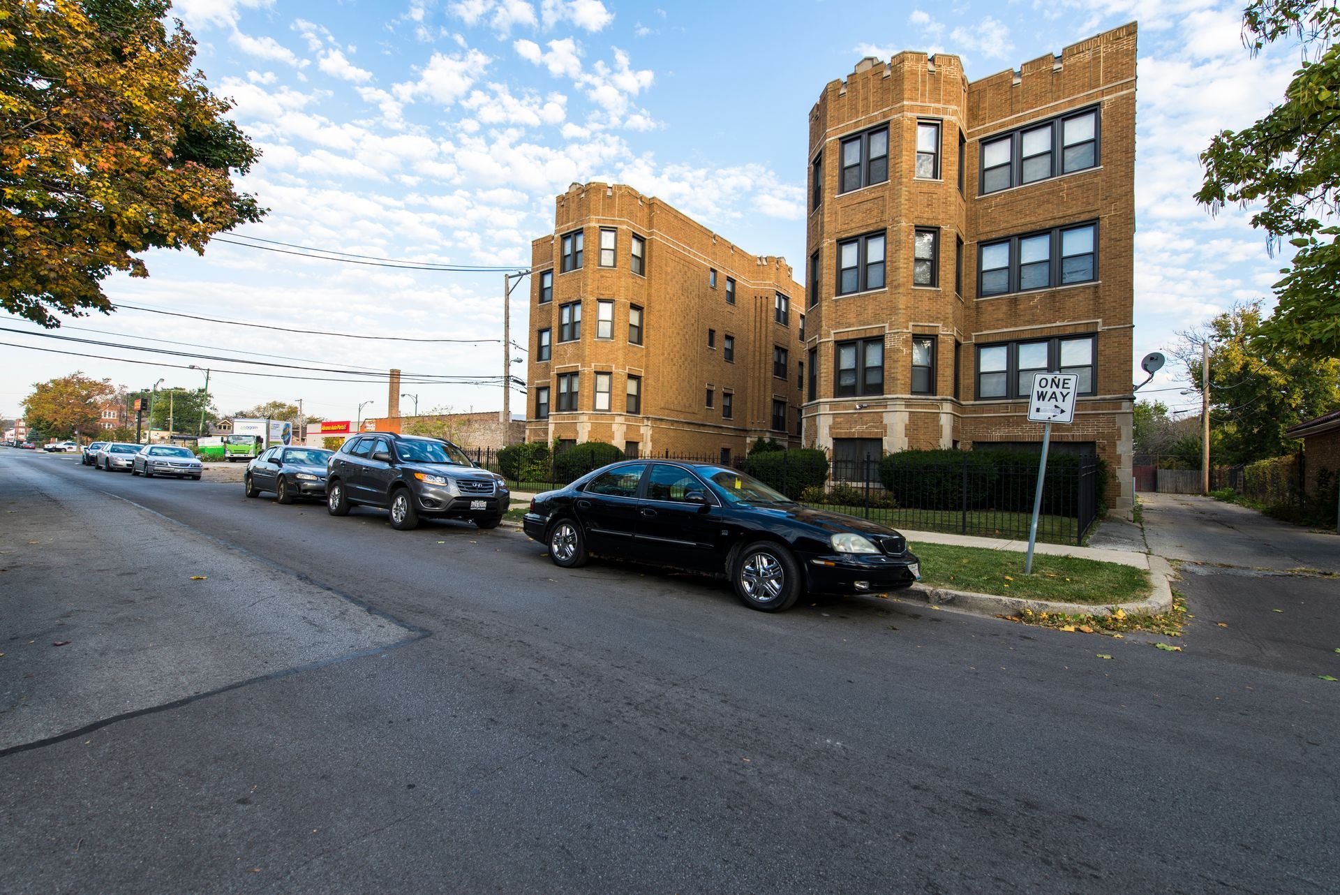 Apartment buildings and parked cars on a city street under a blue sky.