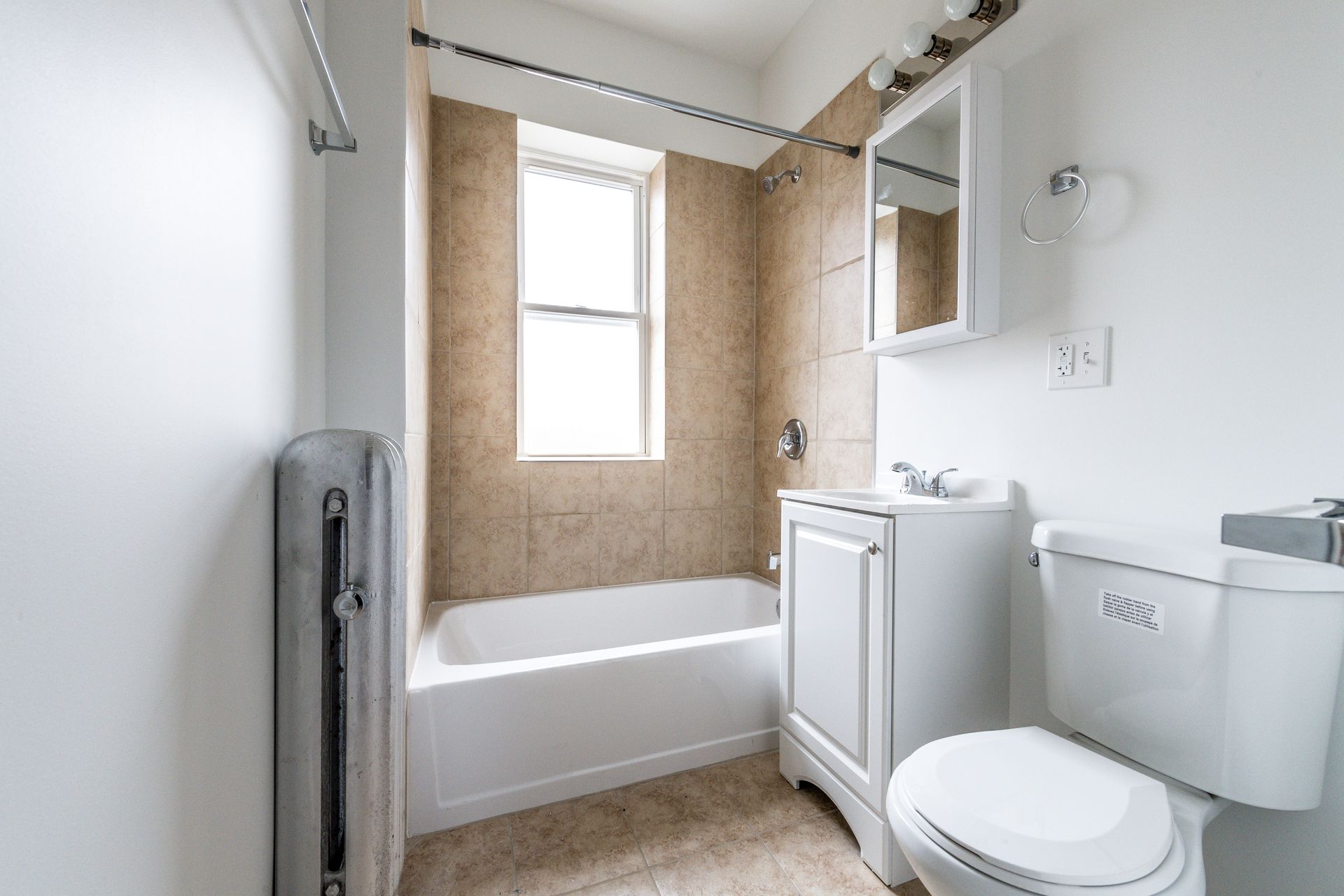 Bathroom with a bathtub, toilet, sink, and window. Beige tile accents and white fixtures.