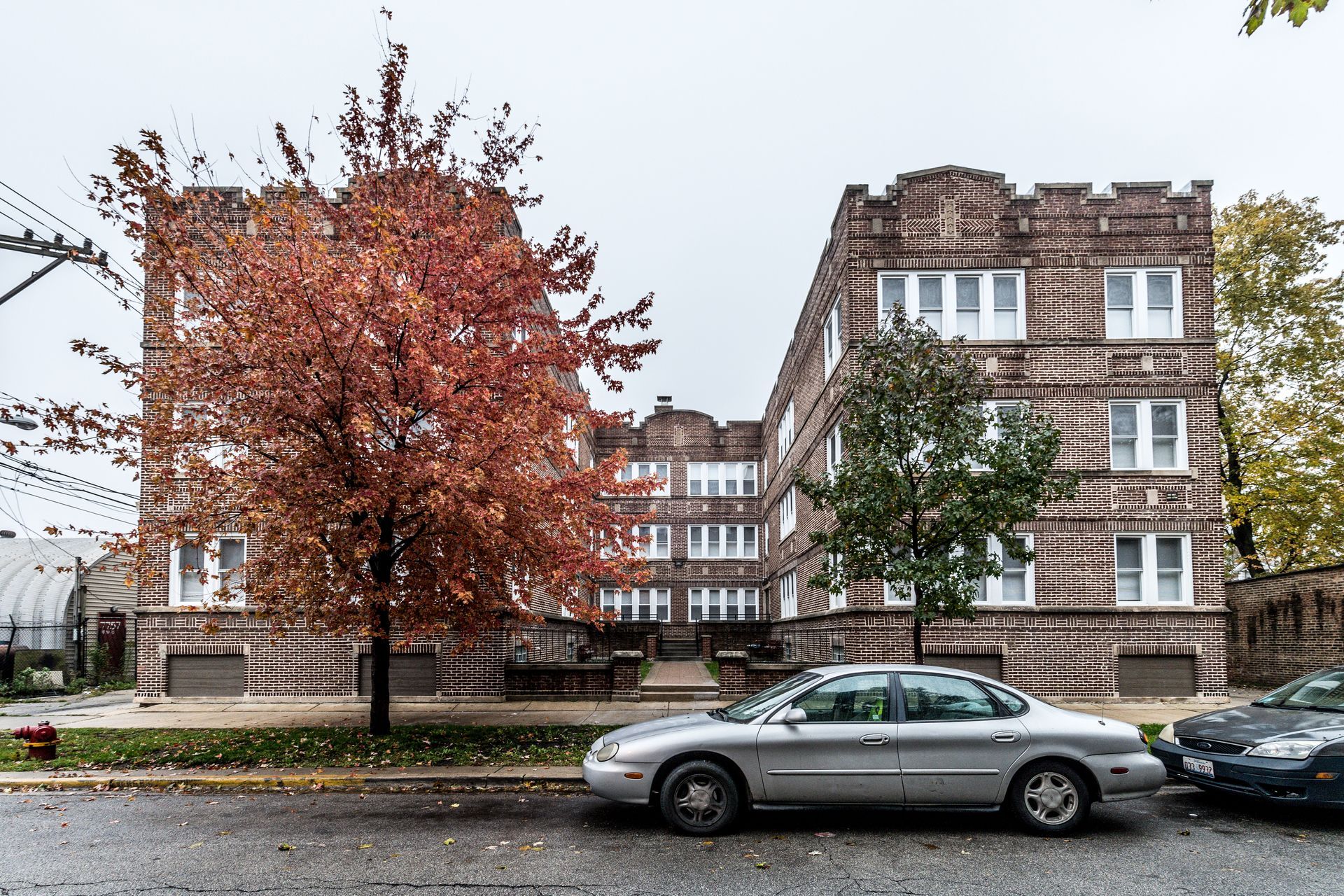 Three-story brick apartment building on a cloudy day with a silver car parked on the street.