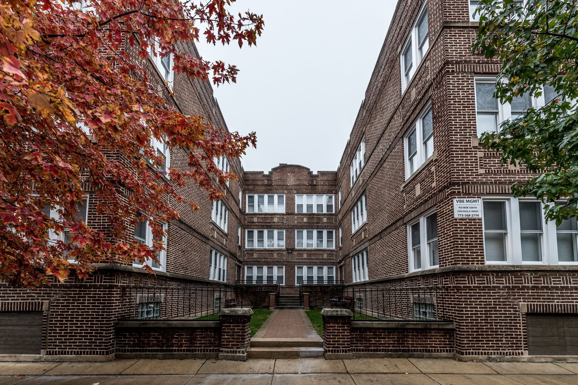 Brick apartment building with red and green trees on a cloudy day.