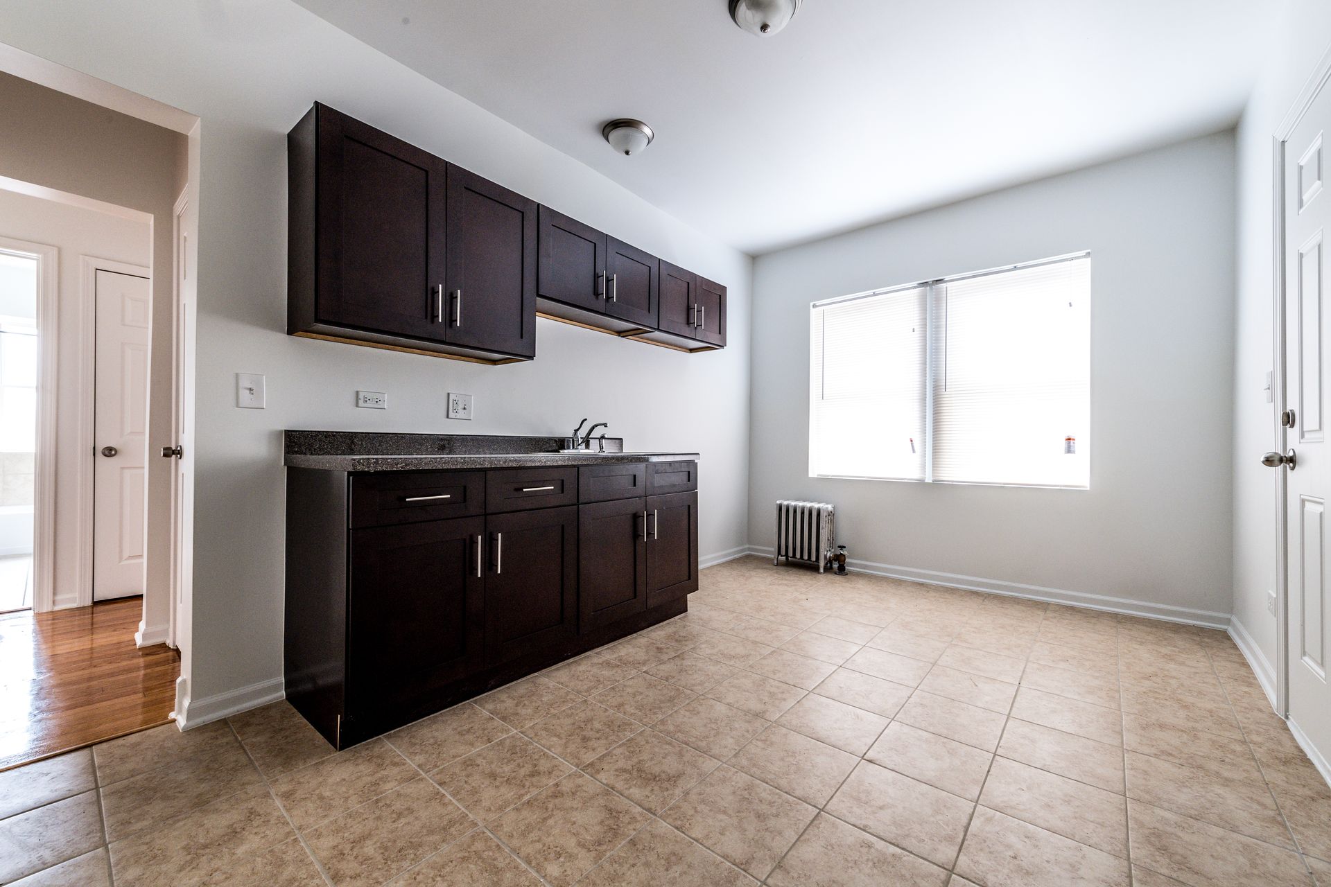 Kitchen with dark cabinets, a sink, and a window. Beige tile flooring.