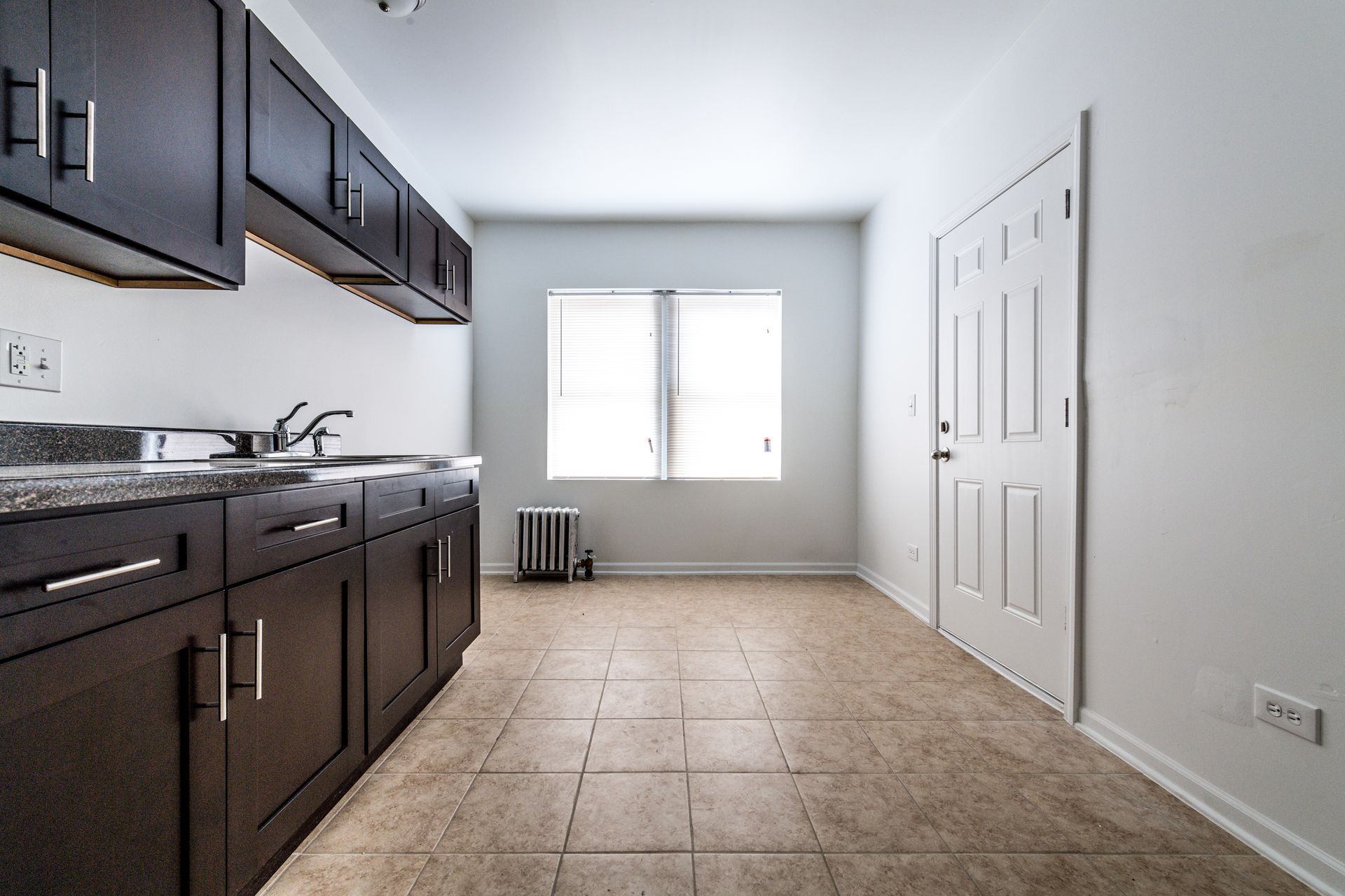 Kitchen with dark brown cabinets, window, and closed white door.