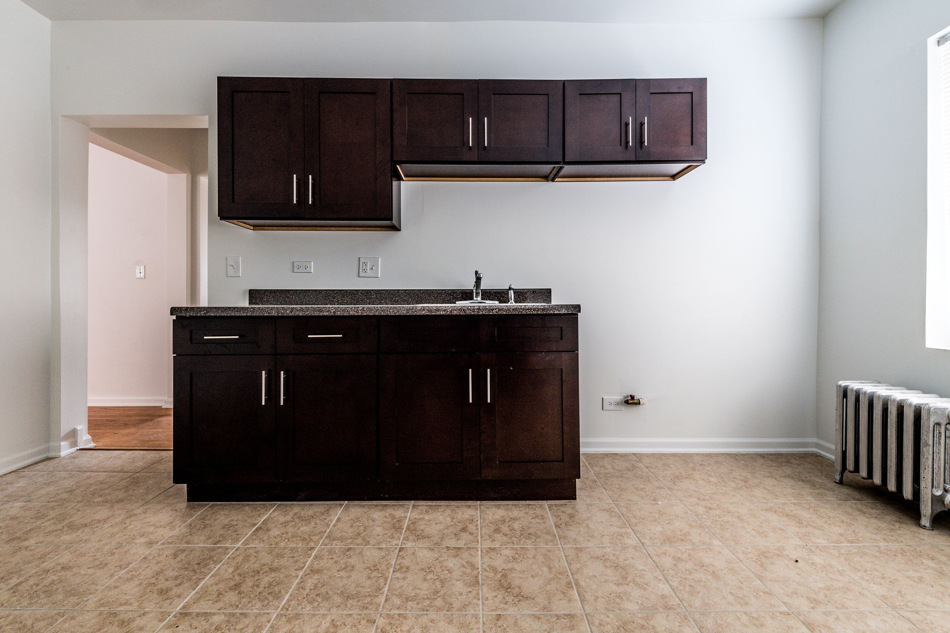 Empty kitchen with dark brown cabinets, granite countertop, and radiator.