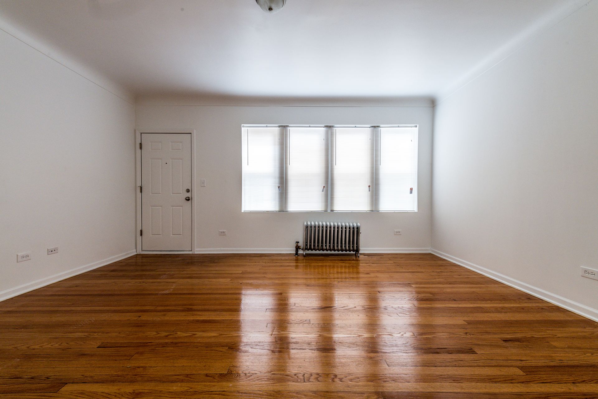 Empty room with hardwood floors, white walls, and a window.