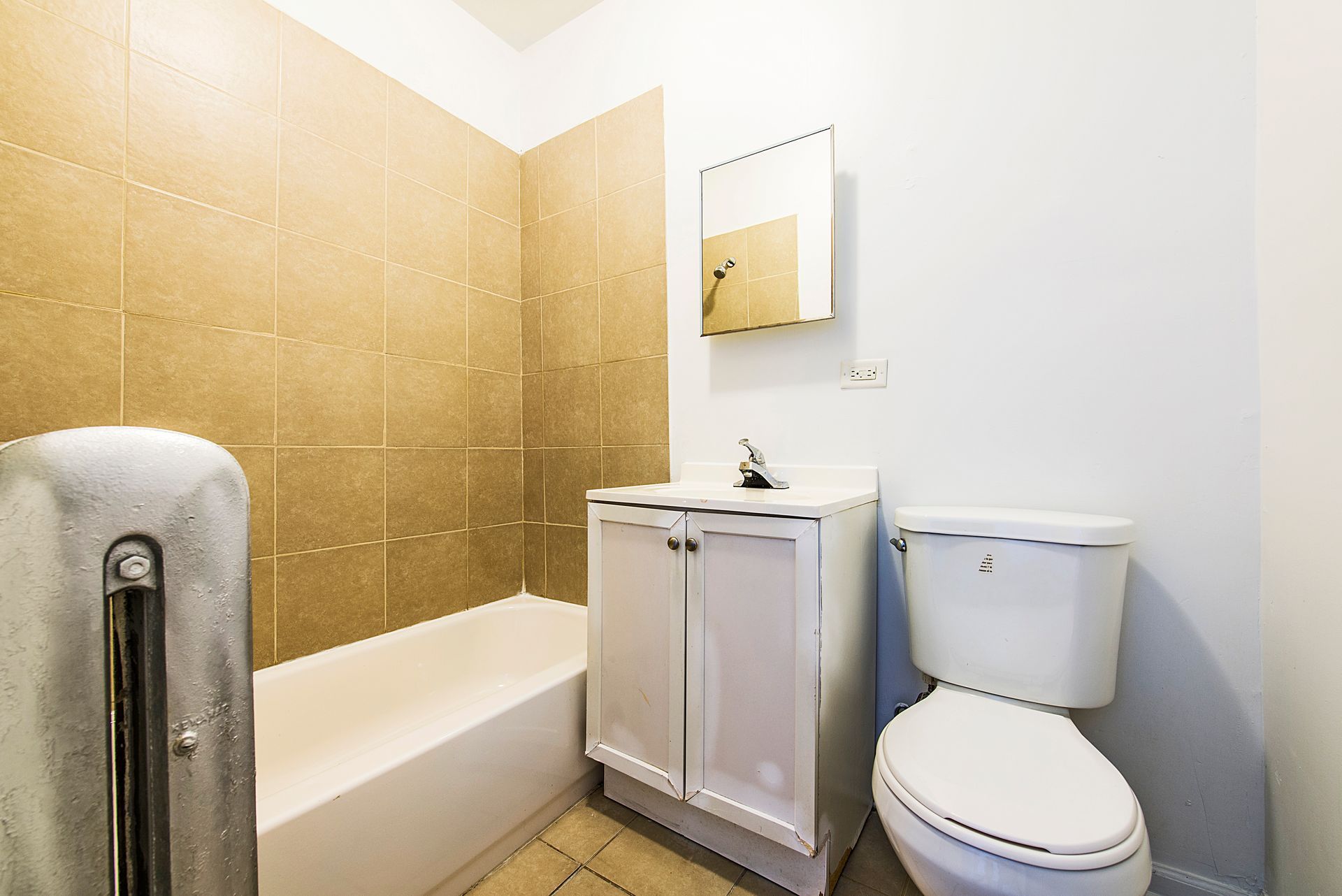 Bathroom with white fixtures, beige tiled wall, white vanity, and a mirror.