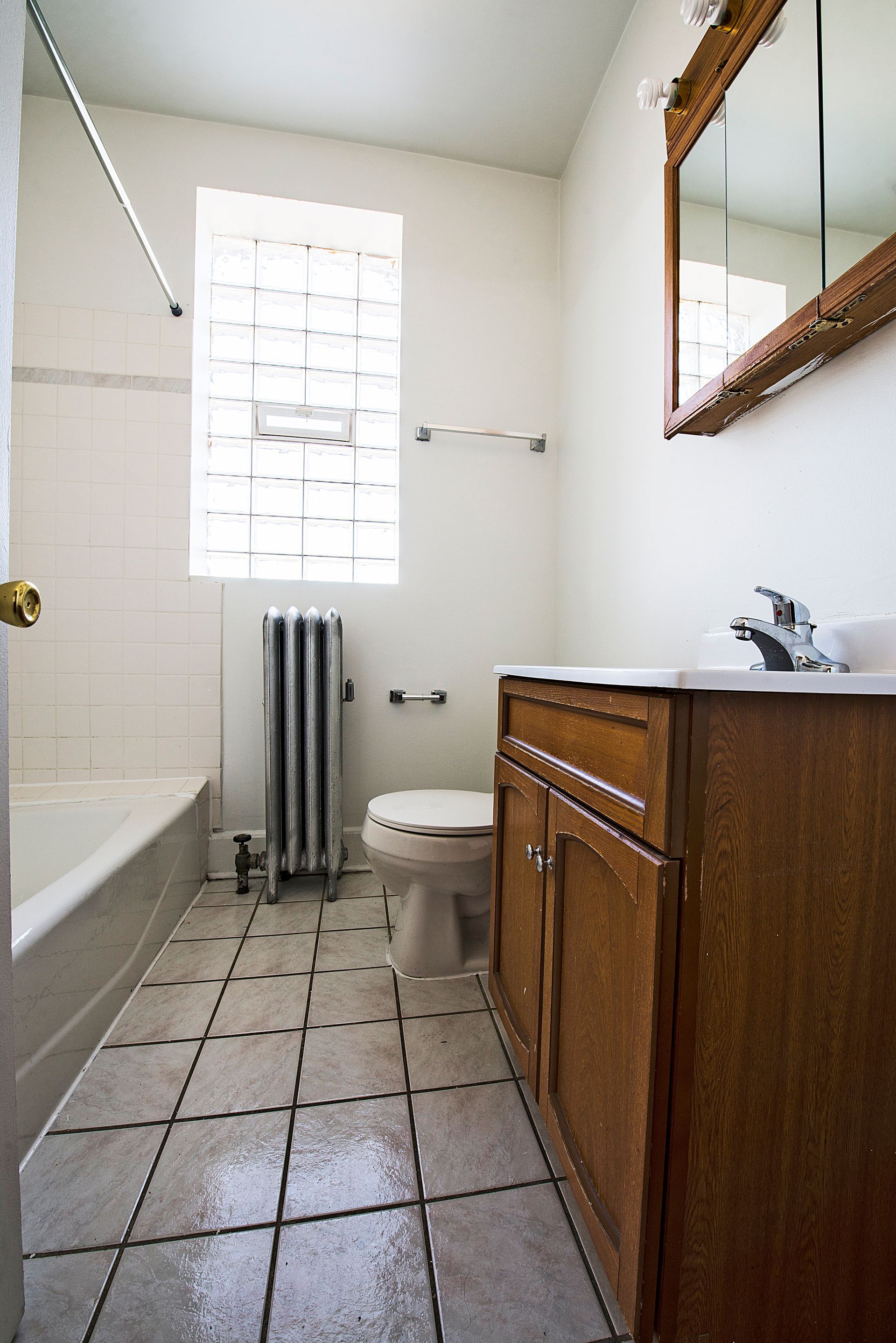 Bathroom with a white bathtub, toilet, and sink with a wooden cabinet. A window allows light.