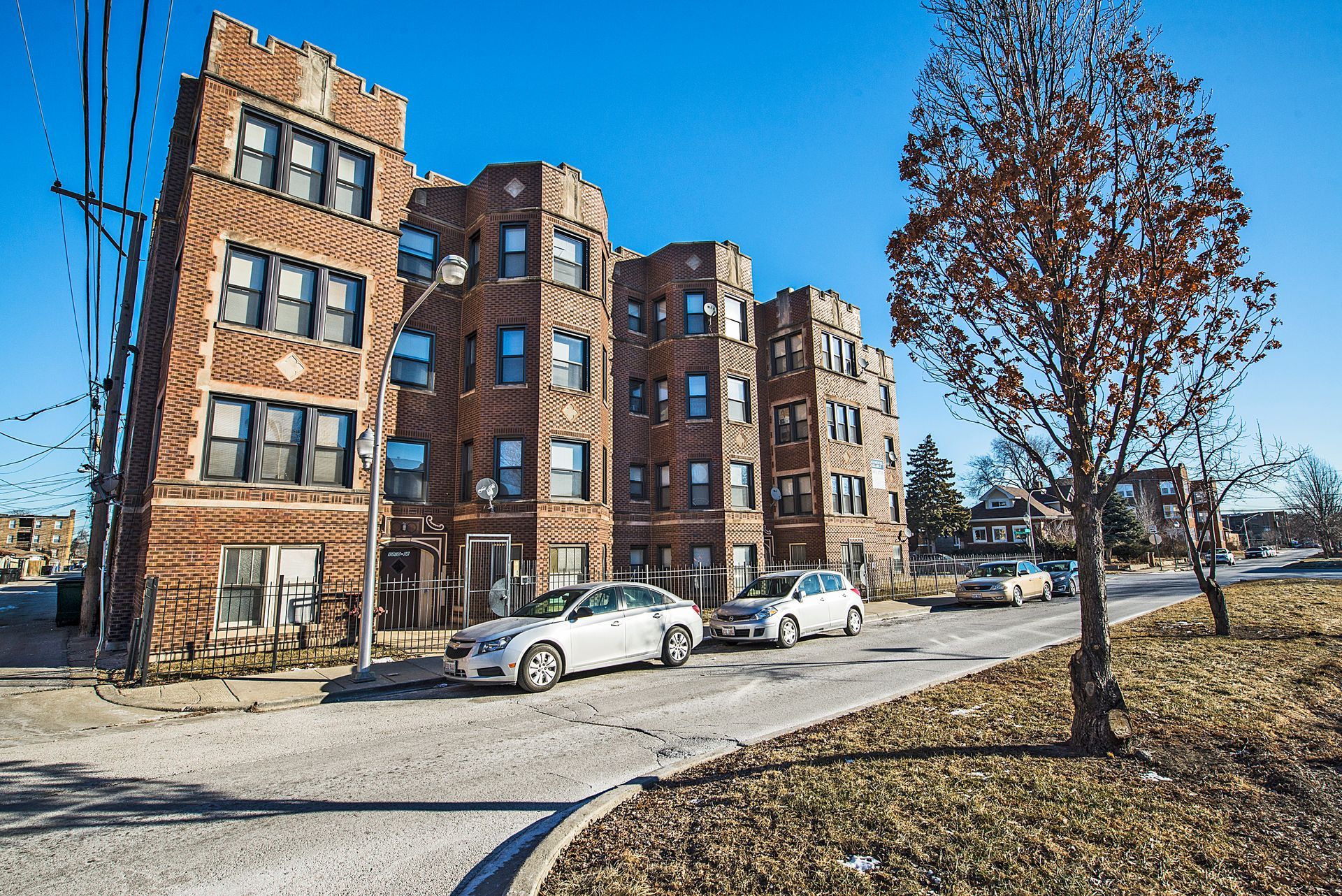 Brick apartment building with parked cars on a sunny day.
