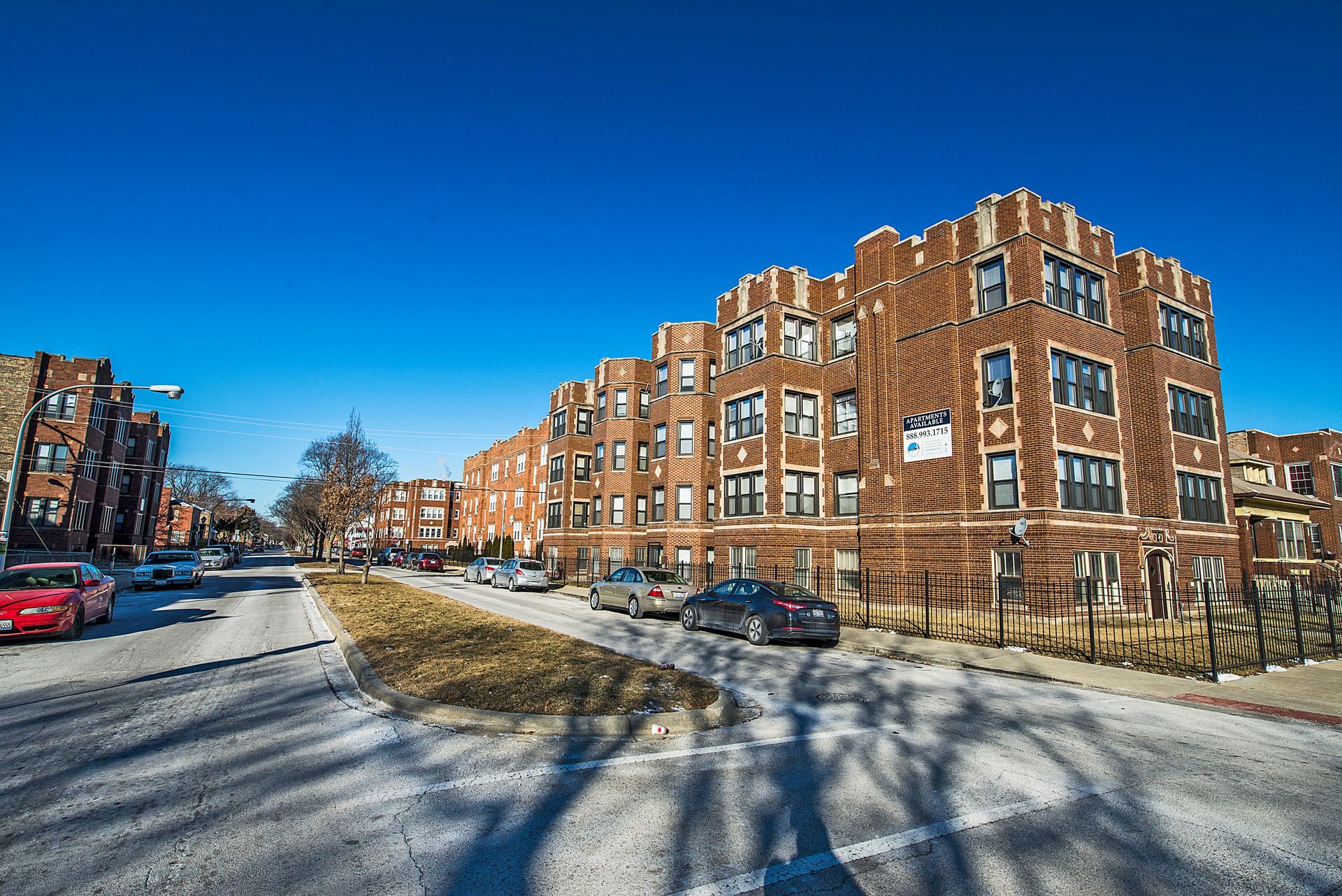 Apartment building on a sunny street with parked cars and clear blue sky.