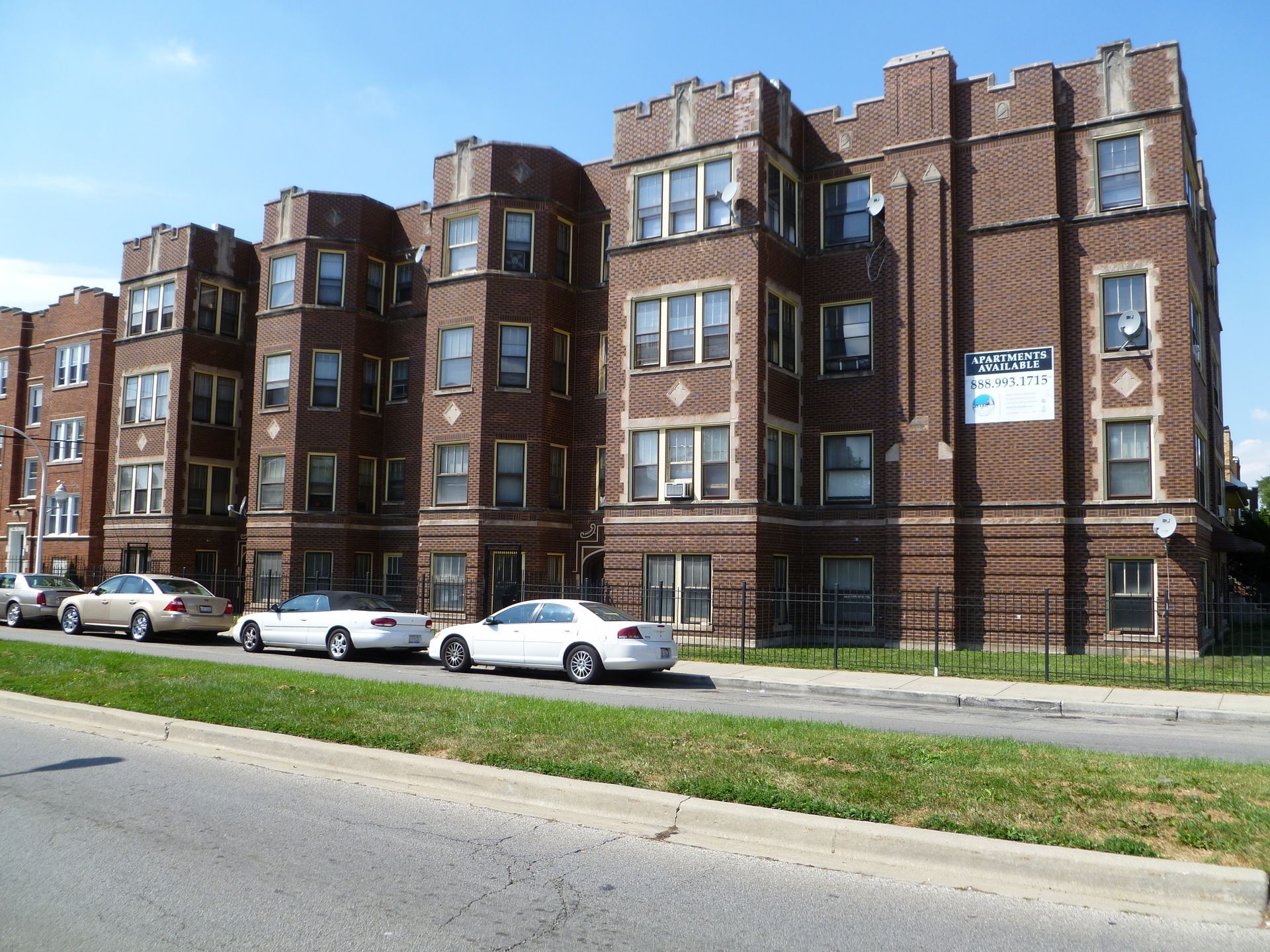 Brown brick apartment building with cars parked on the street.