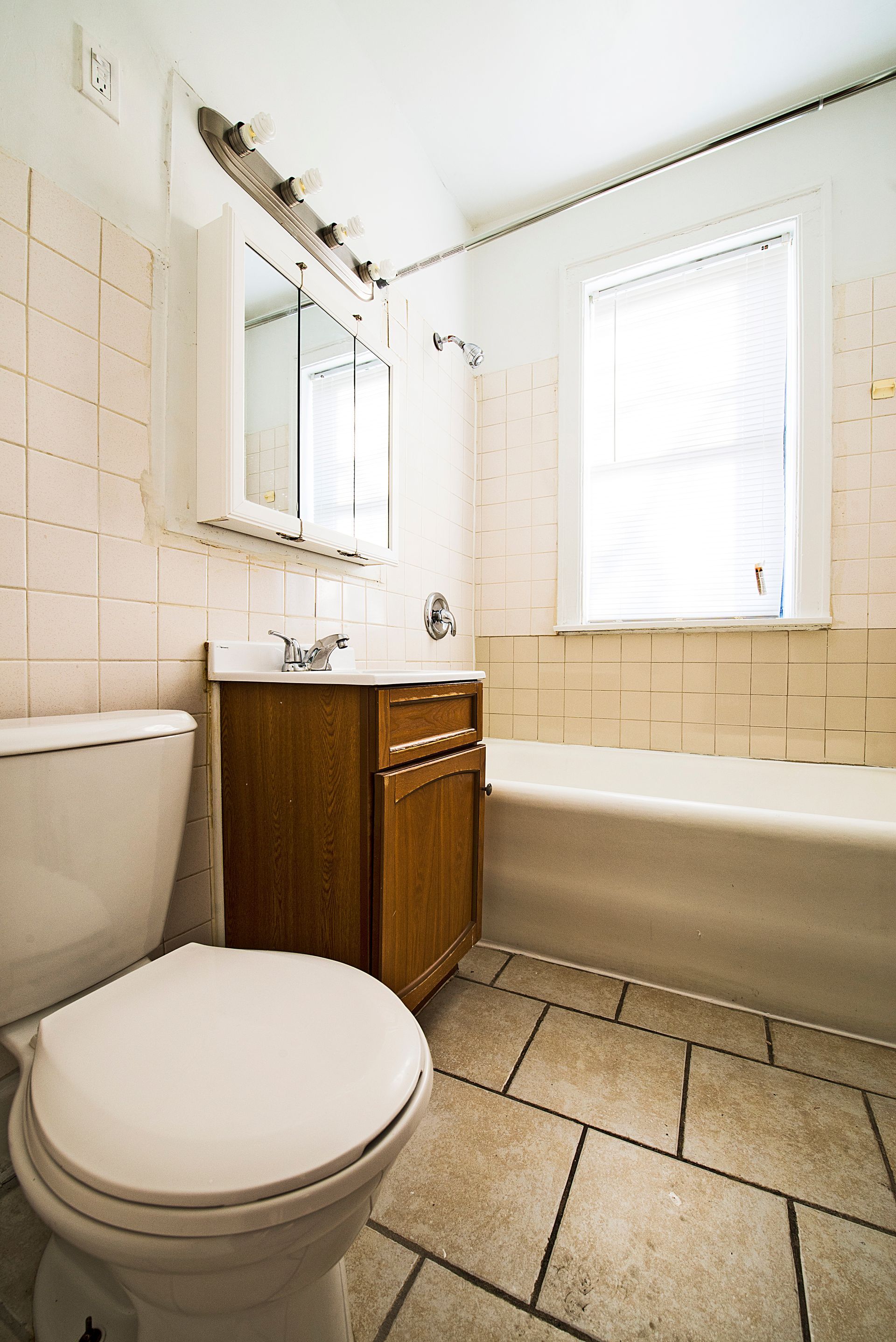 Bathroom with toilet, sink, tub, and window; beige and brown tones.