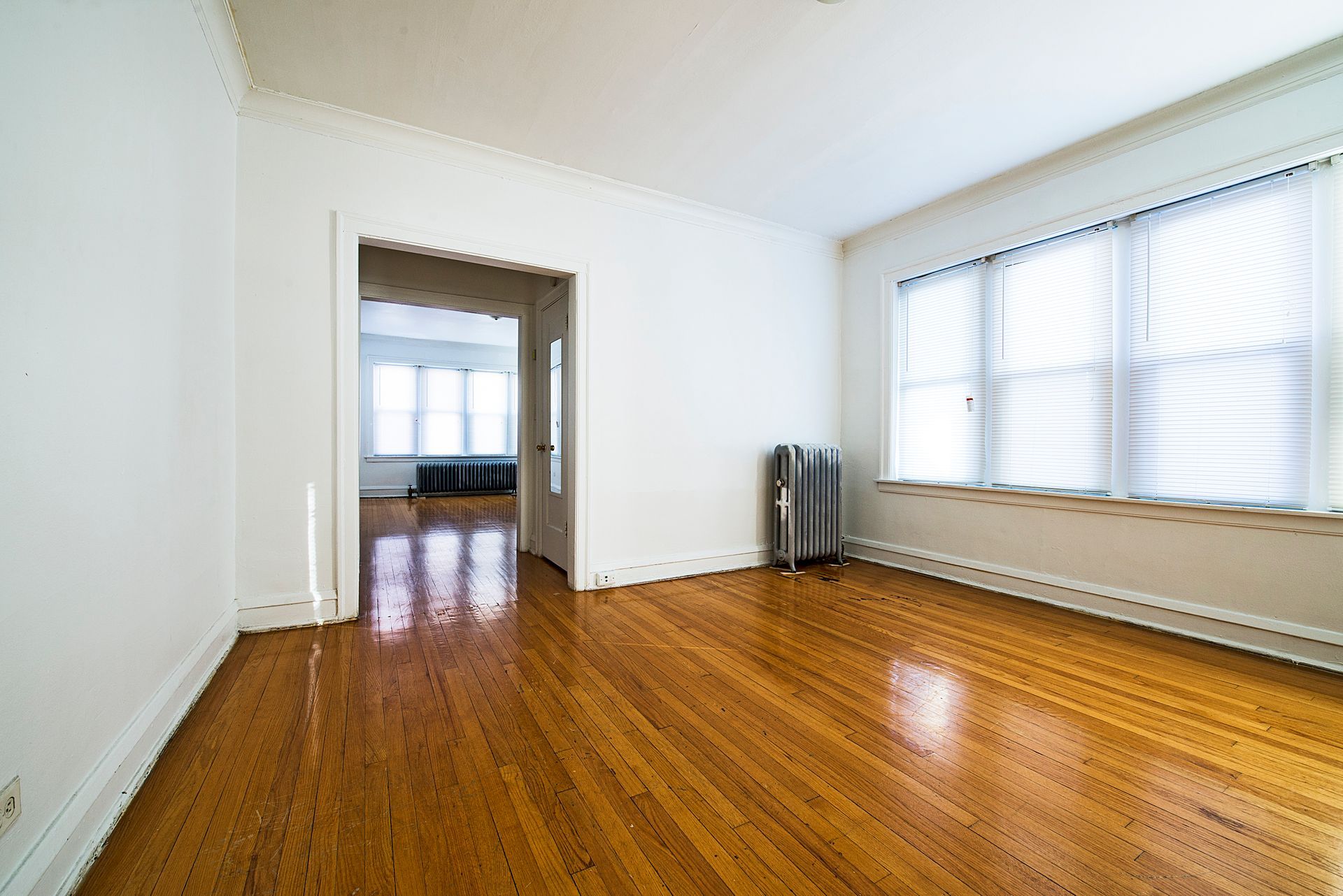 Empty room with hardwood floors, a large window, and a doorway to another room.