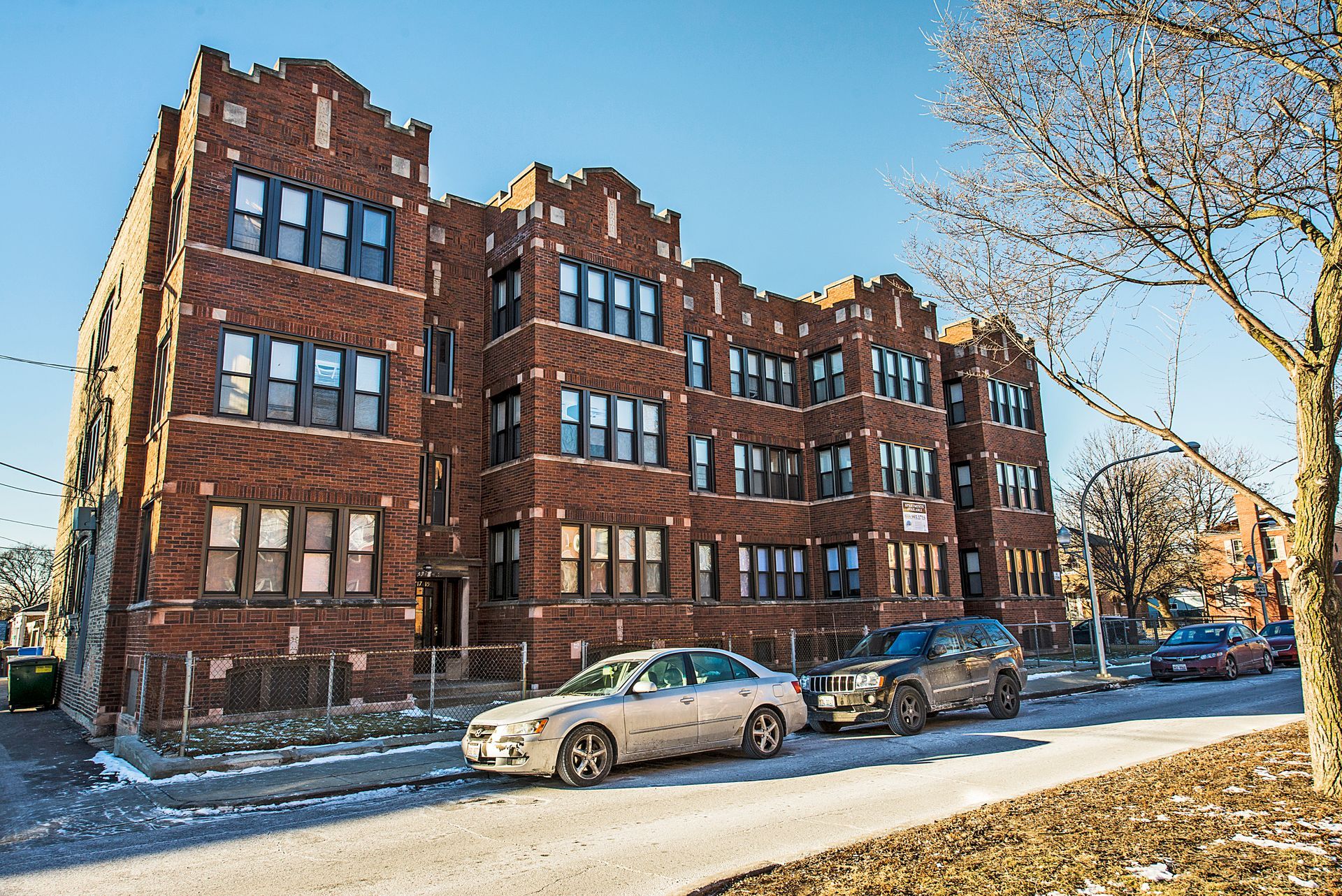 Brick apartment building on a sunny winter day, cars parked on street.
