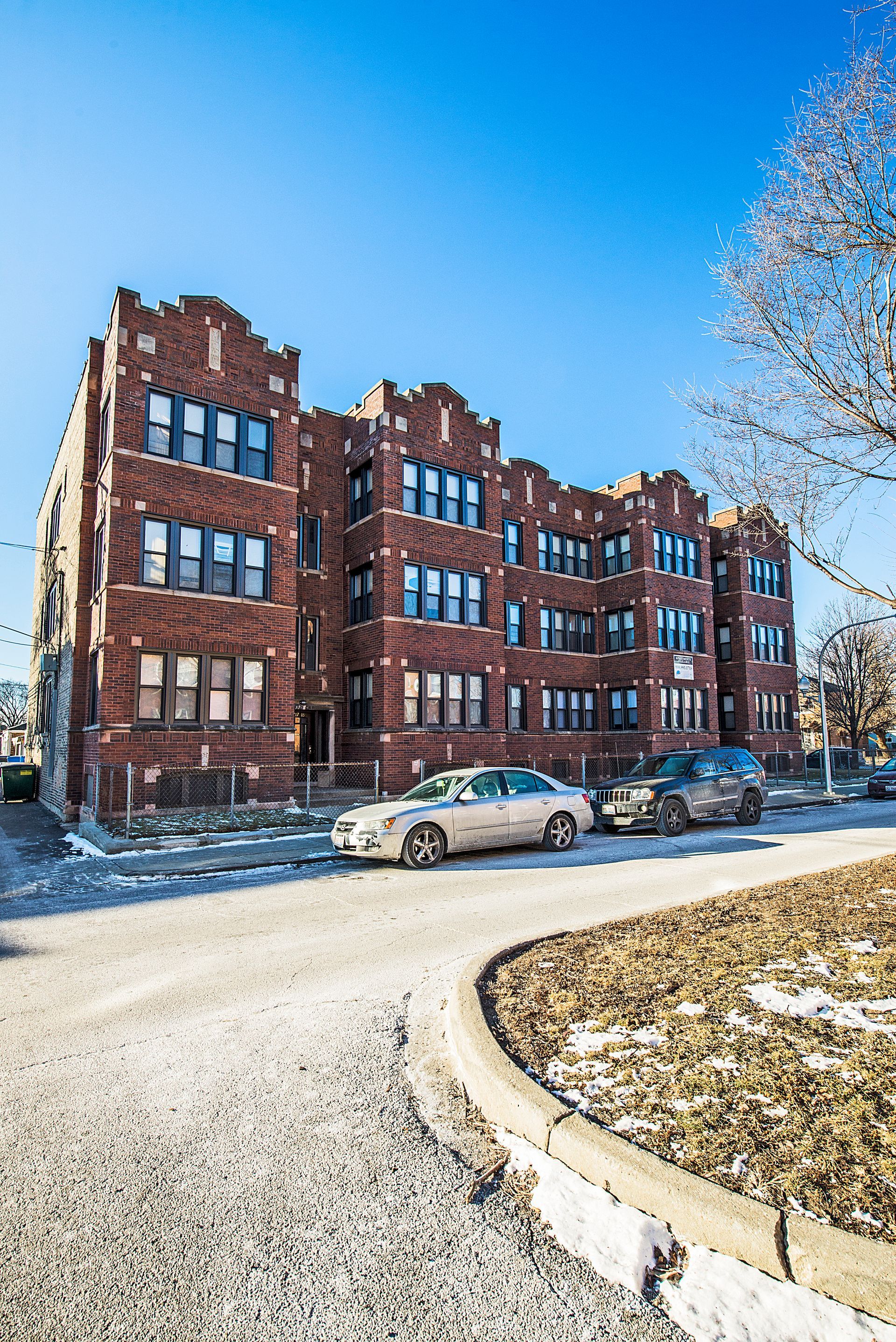 Brick apartment building with parked cars on a winter day.