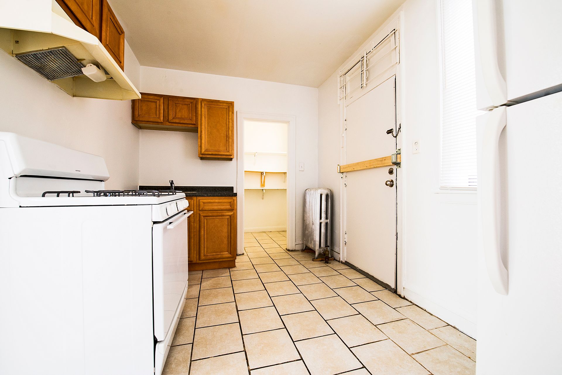 Kitchen with white appliances, wooden cabinets, and tile floor, leading to a pantry.