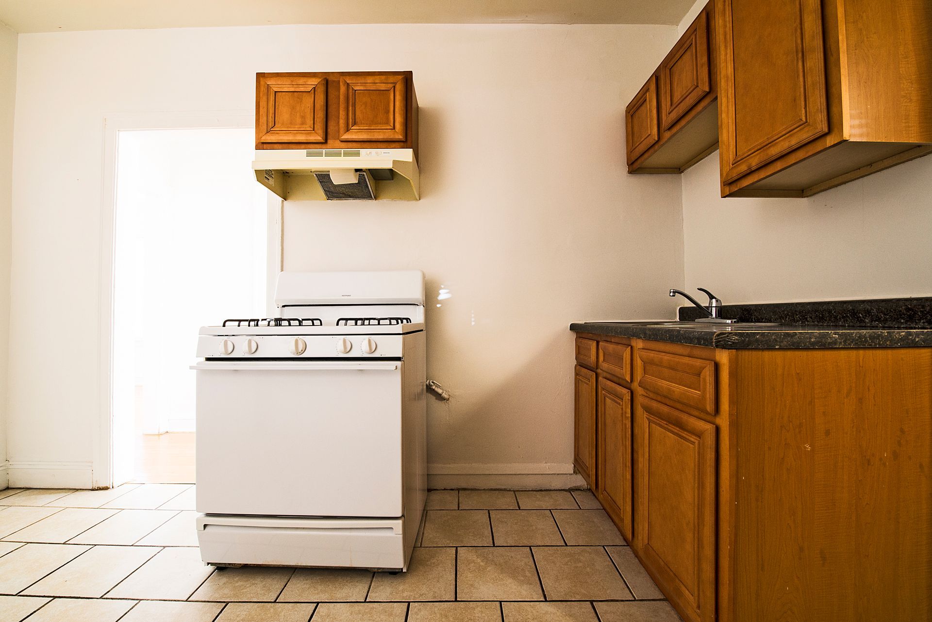 Empty kitchen with light brown cabinets, white stove, and off-white walls.