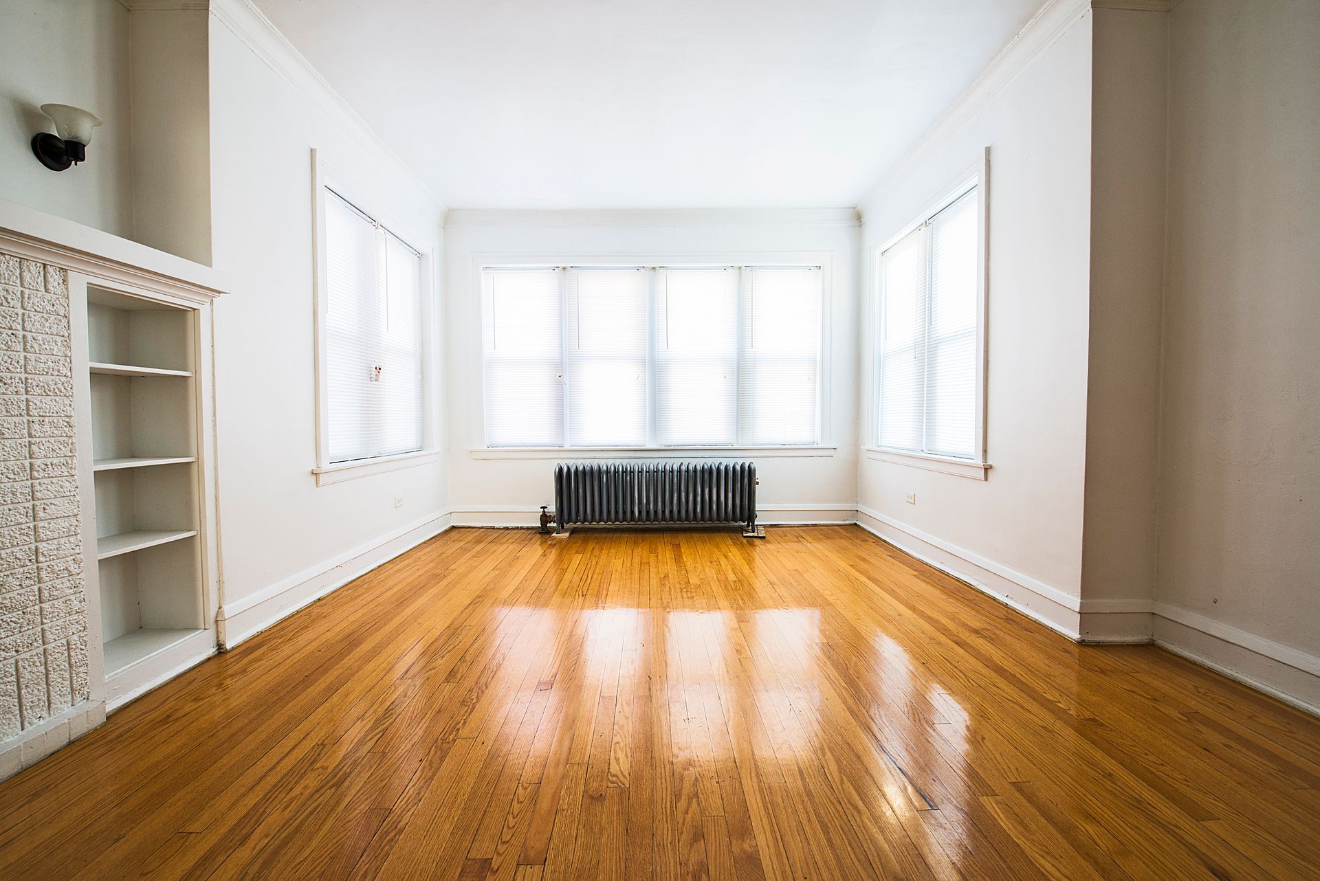 Empty room with hardwood floors, windows, and built-in white bookshelf.