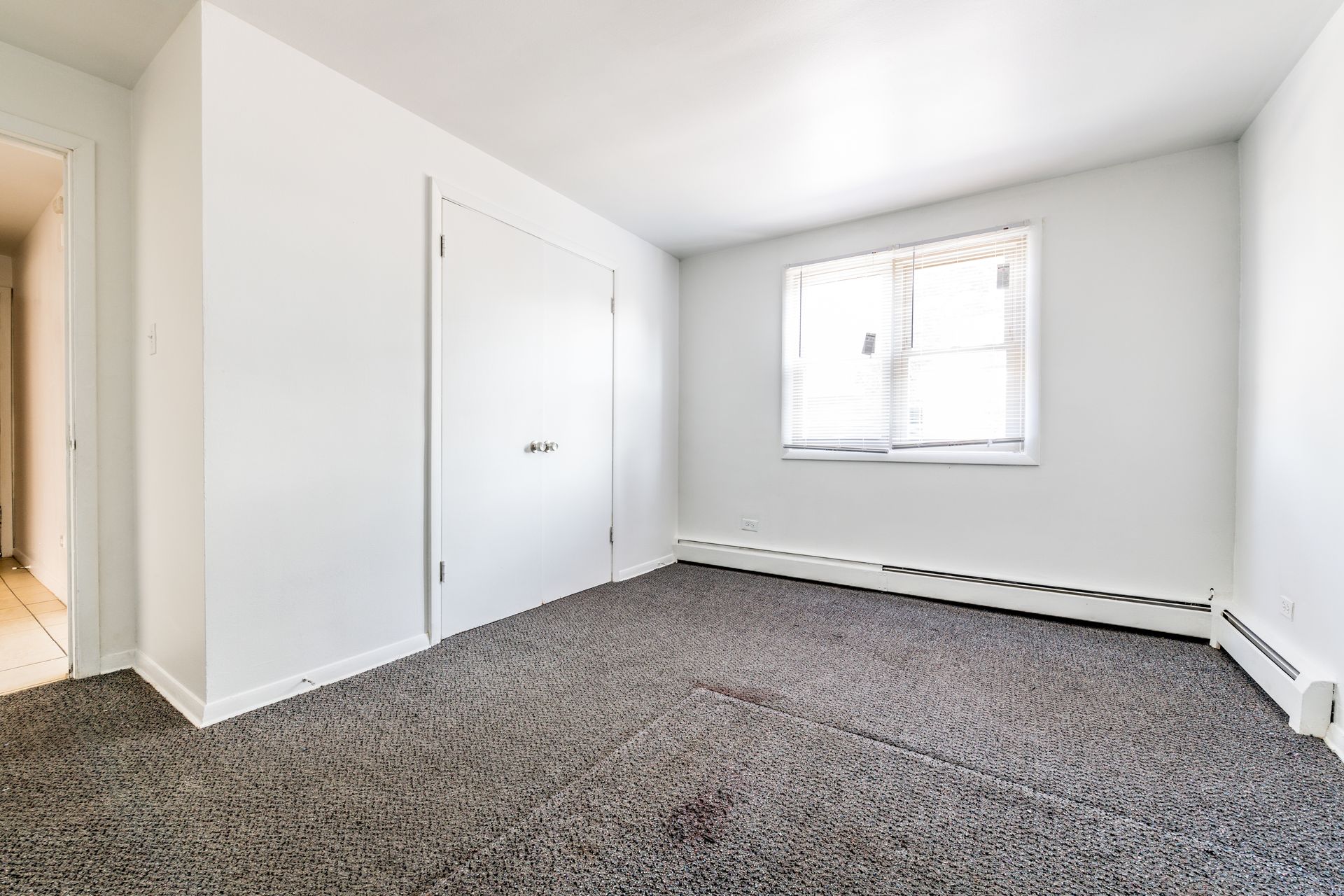 Empty bedroom with gray carpet, white walls, closet, and window.