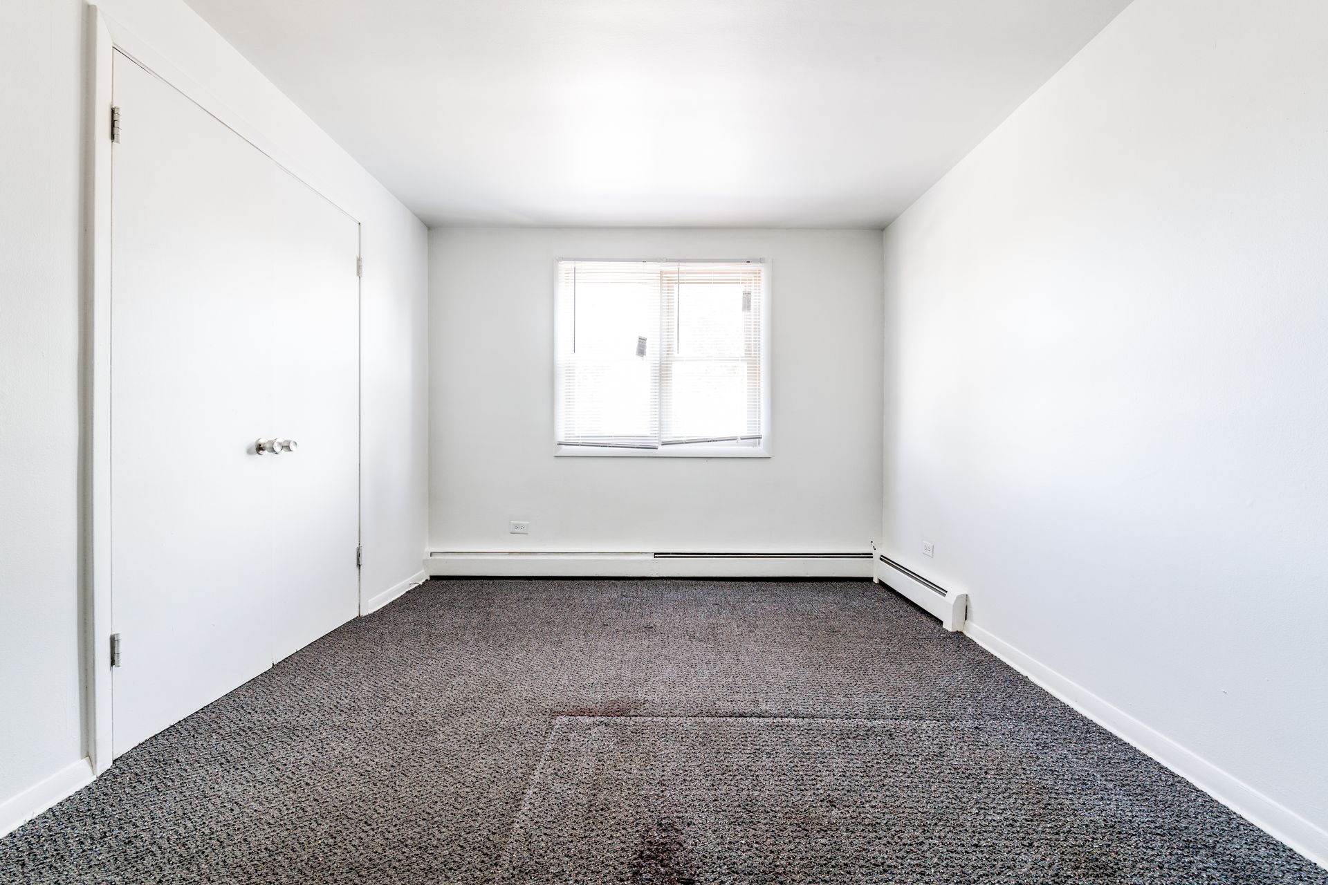 Empty room with white walls, carpeted floor, window, and closet doors.