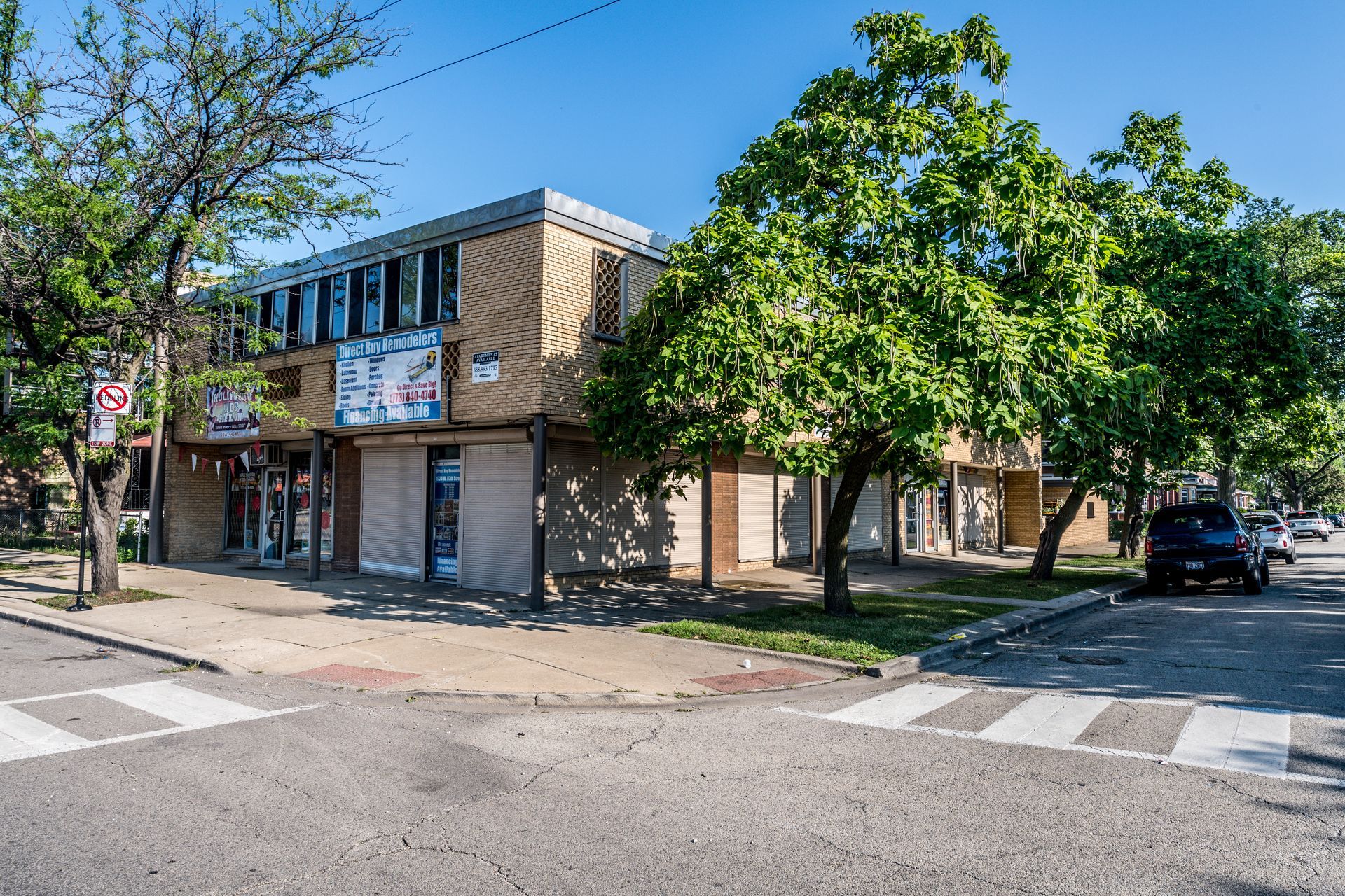 Two-story commercial building on a corner lot, with trees and a parked car.