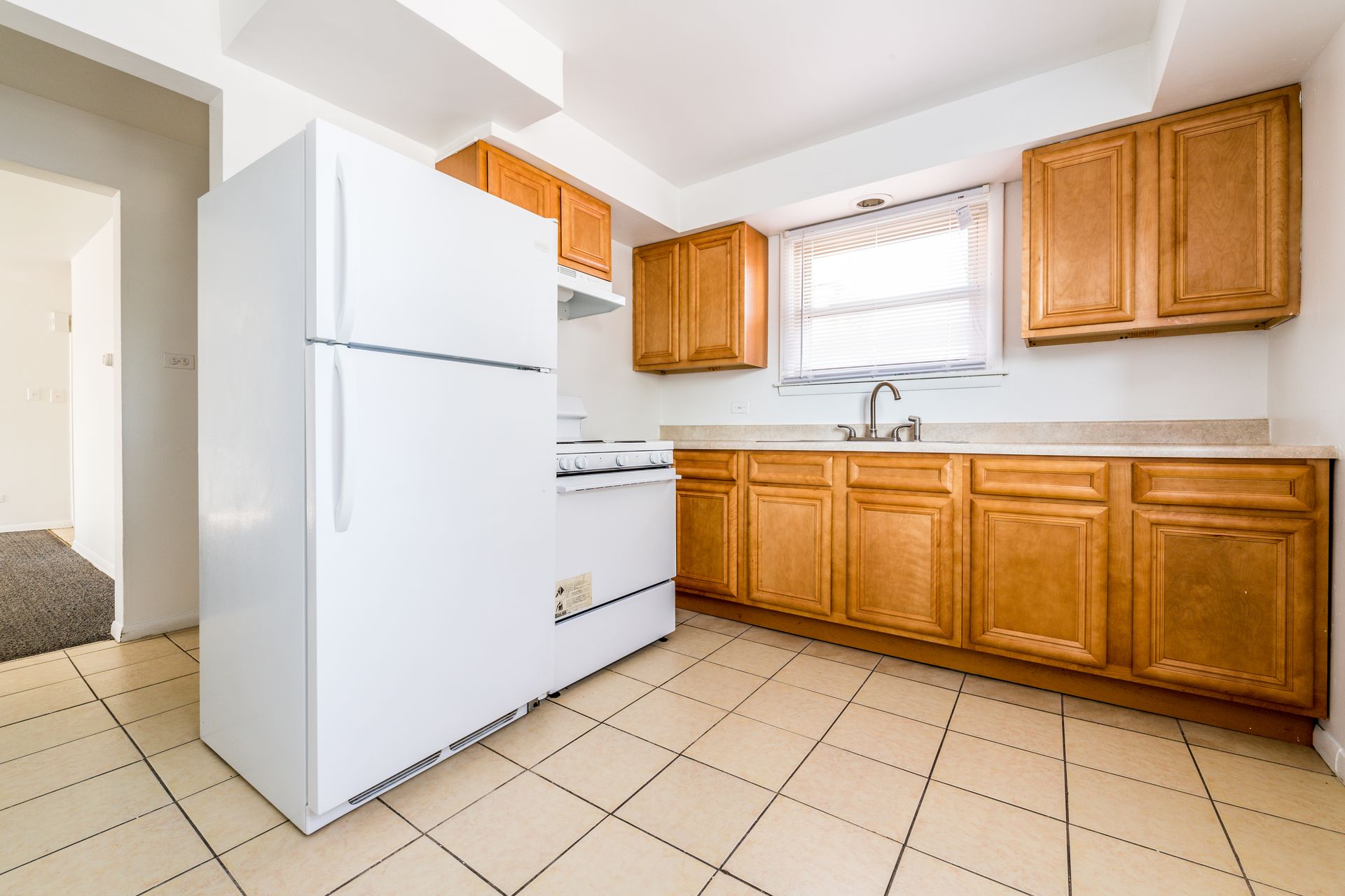 Kitchen with white appliances, light wood cabinets, and beige tiled floor.