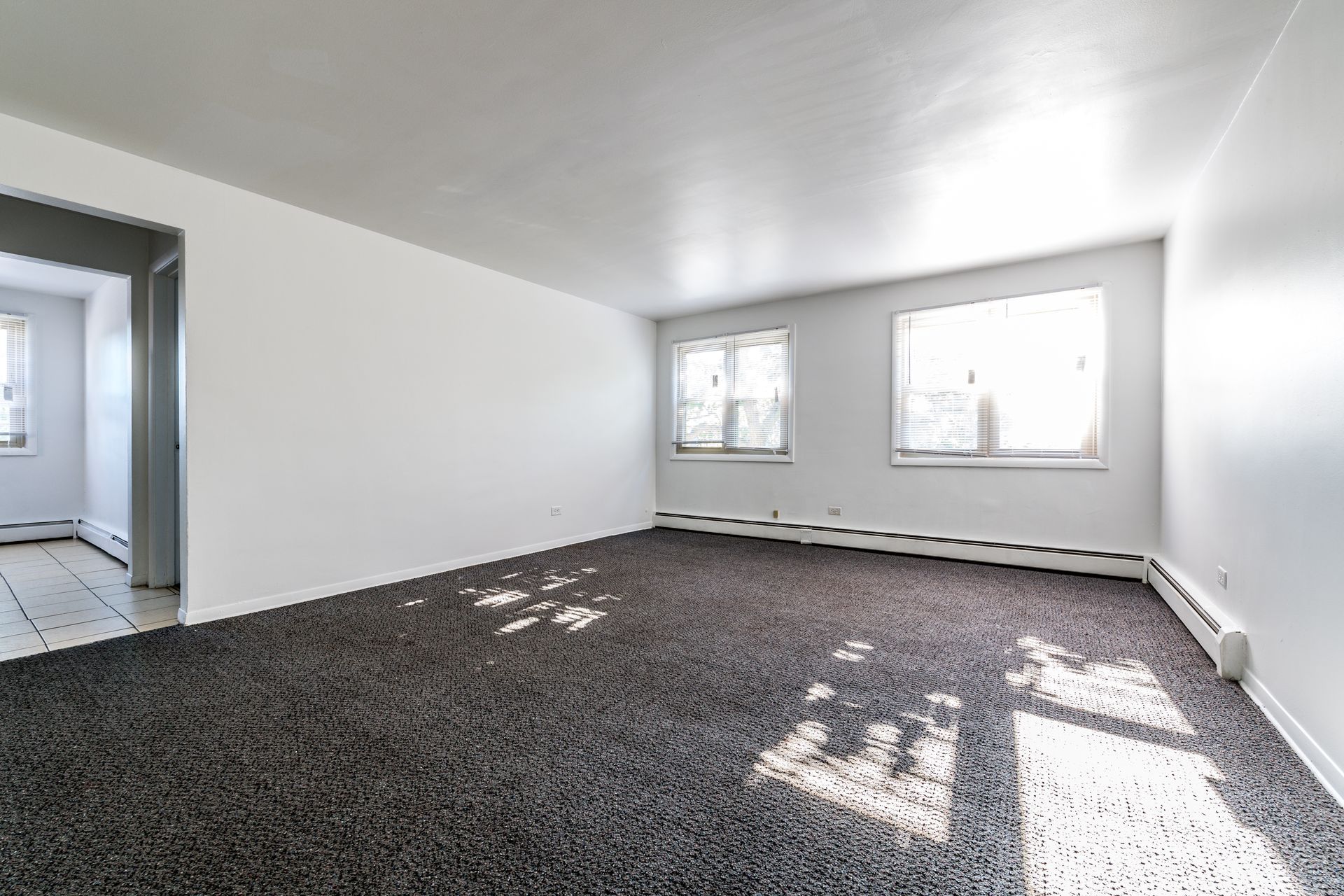 Empty room with gray carpet, white walls, and two windows.
