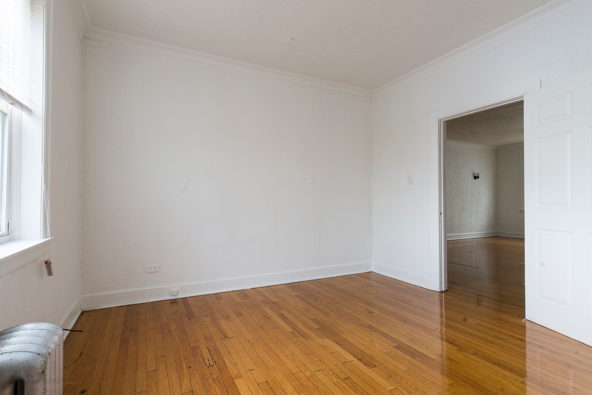 Empty room with hardwood floors, white walls, and a doorway.