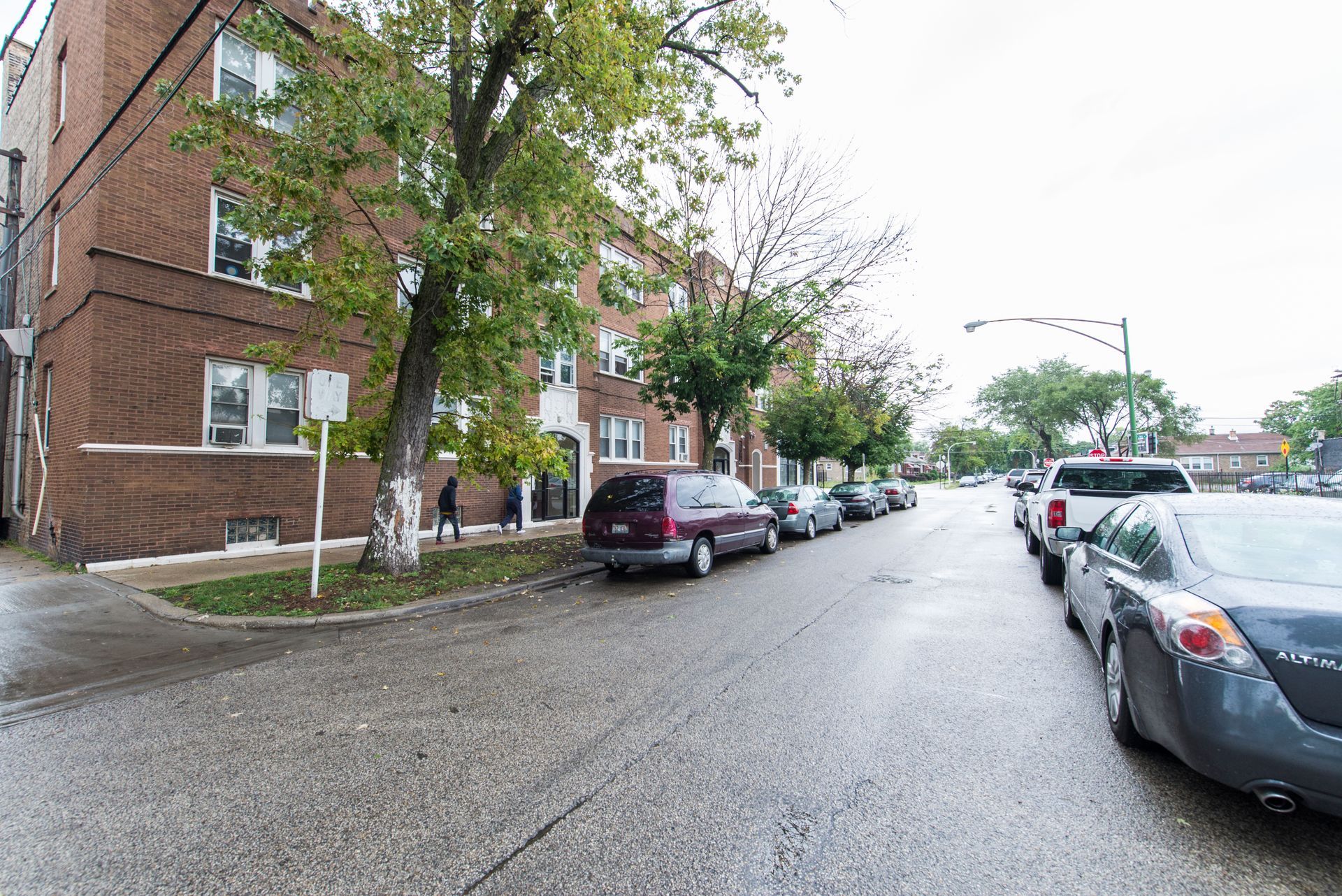 Brick apartment building and parked cars on a wet street on an overcast day.
