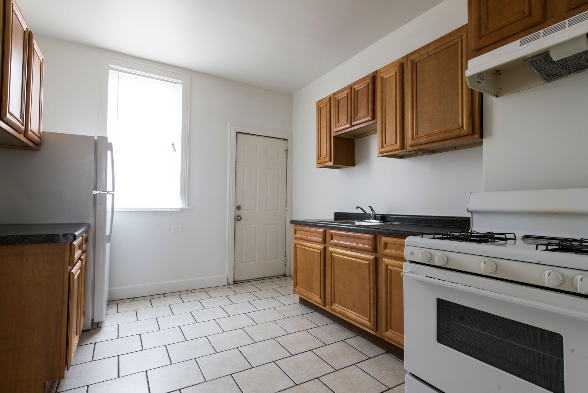 Kitchen with wooden cabinets, white appliances, and a tiled floor. A window lets in light.