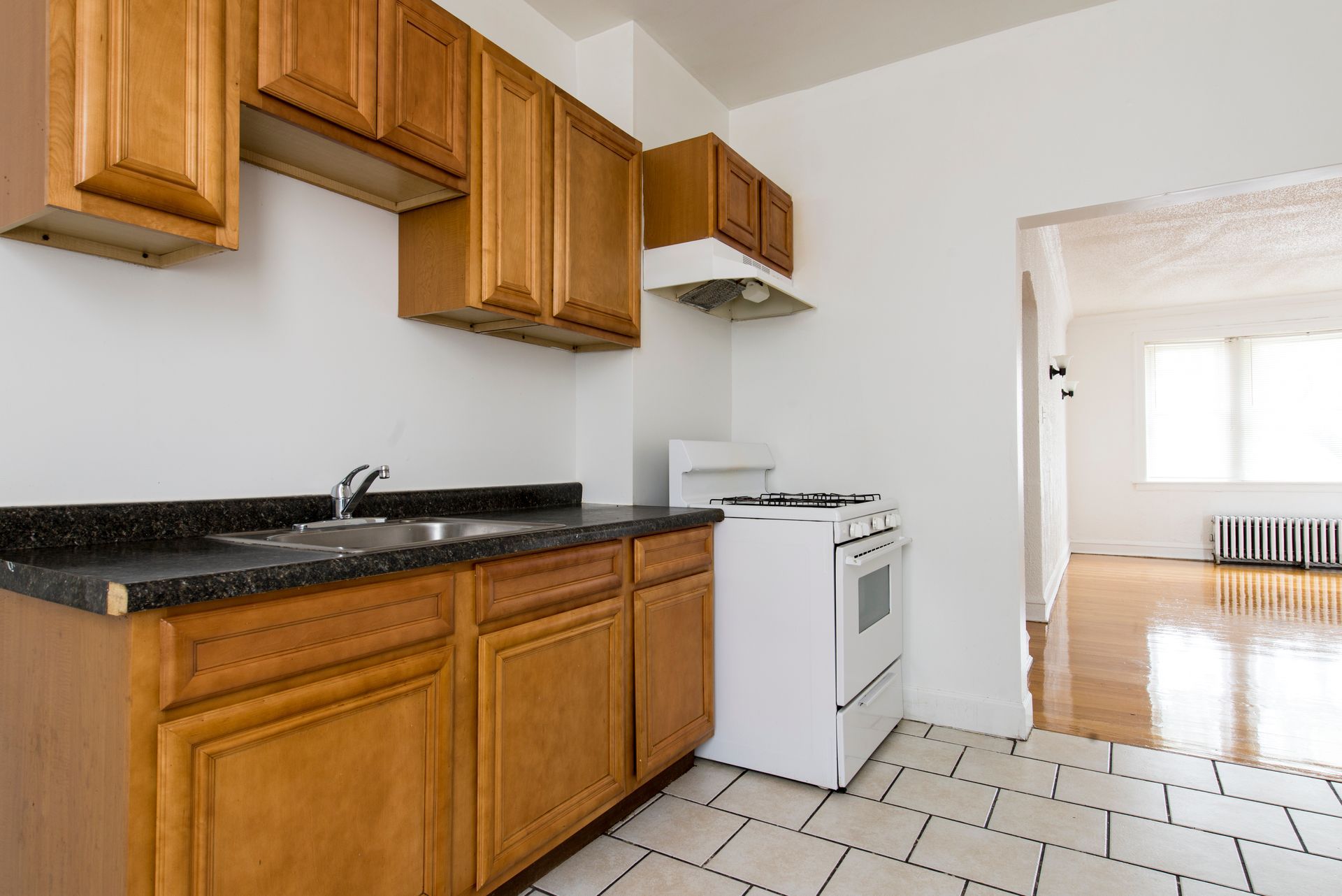 Kitchen with wood cabinets, black countertops, white appliances, and tiled floor; doorway to another room.